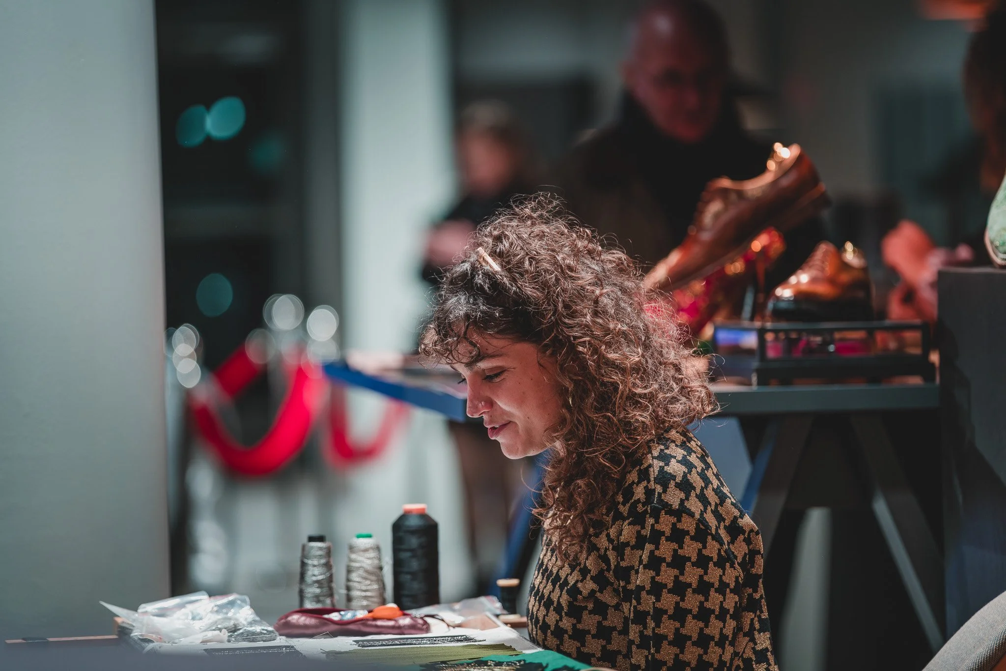 Une femme avec des cheveux bouclés travaillant sur un projet de couture ou de couture, avec des bobines de fil sur la table devant elle, dans un environnement intérieur.