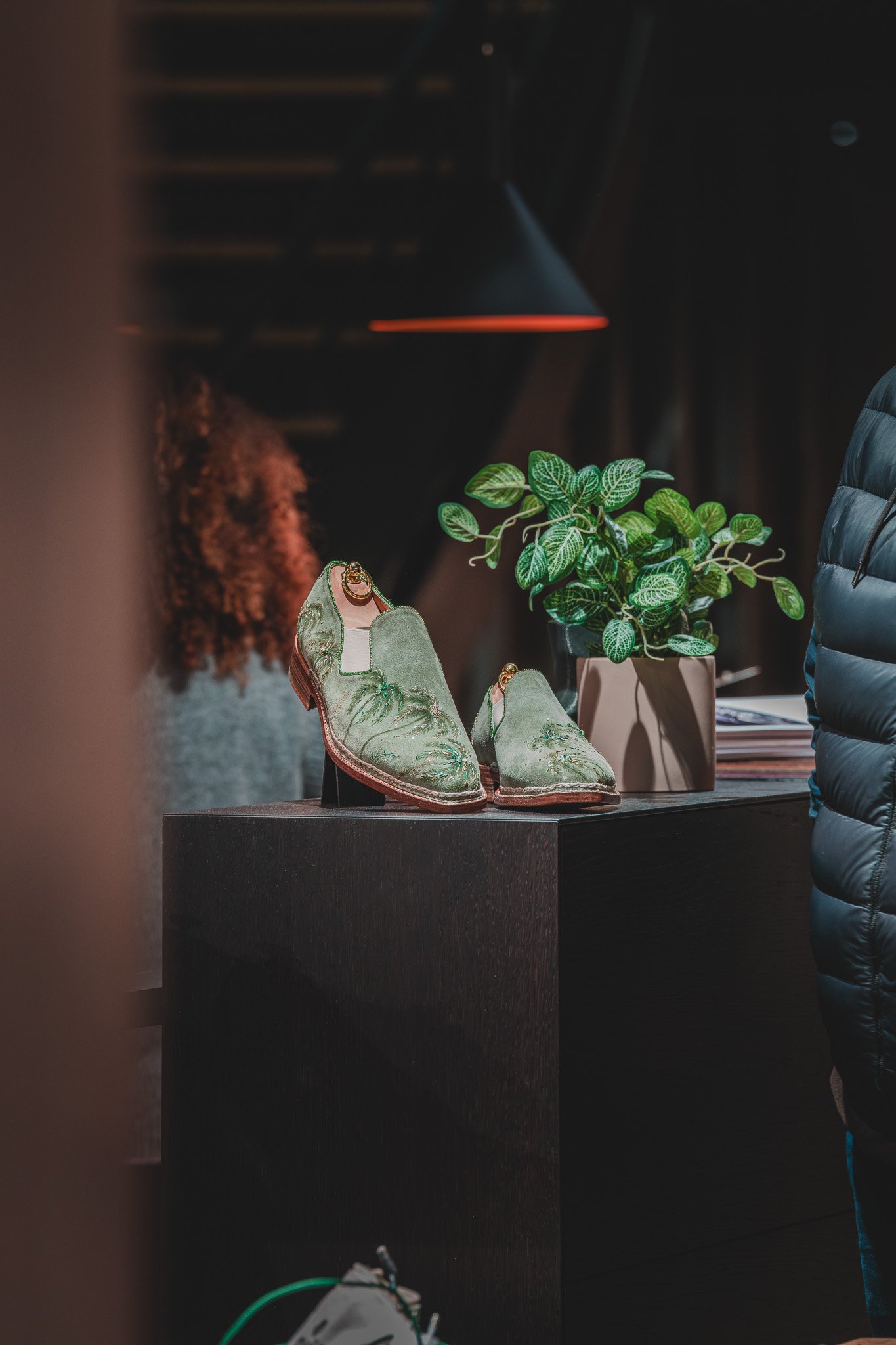 Chaussures vertes en velours sur une table noire, avec une plante verte en pot à côté.