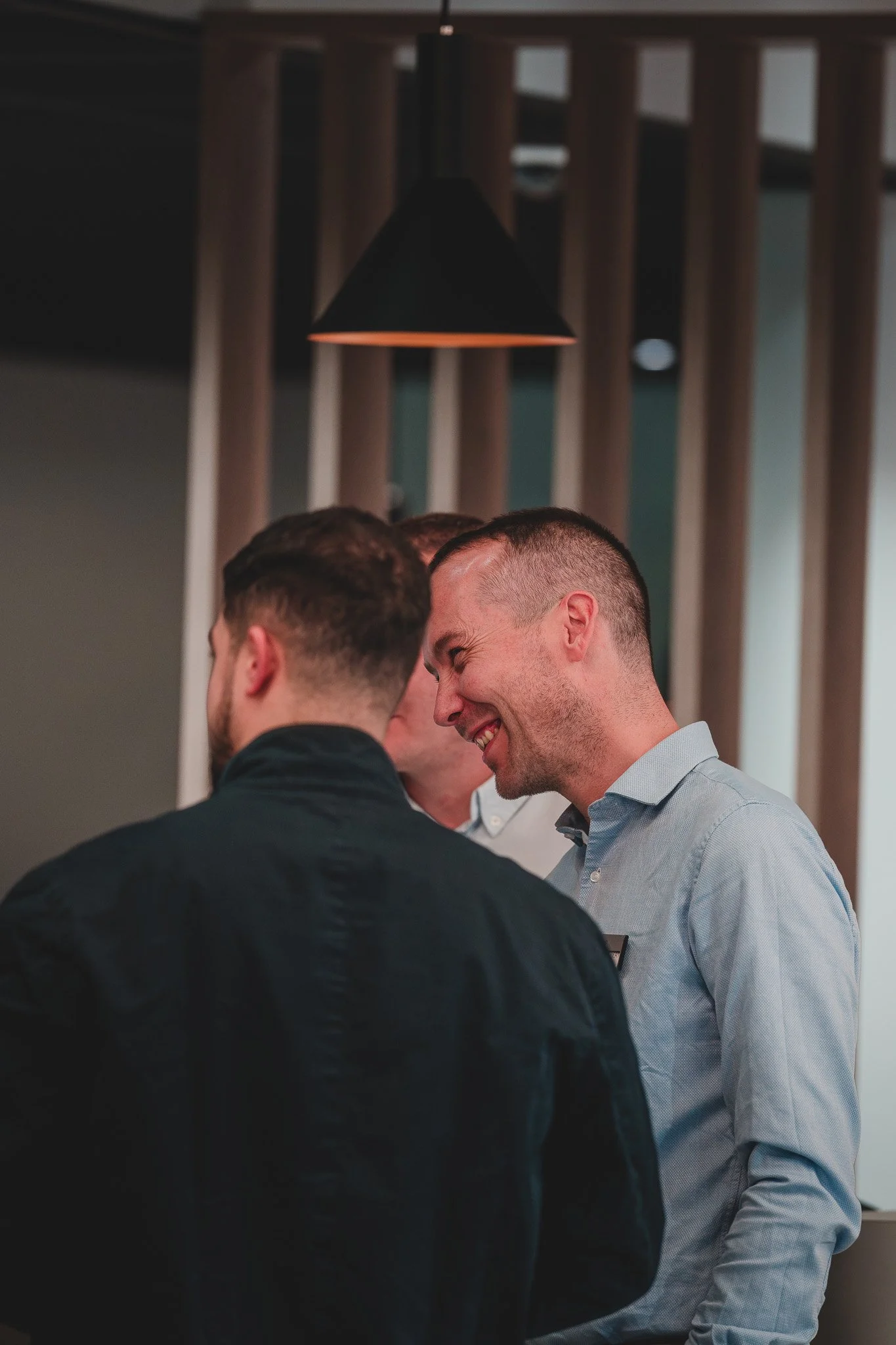 Groupe de trois hommes souriants en conversation dans un intérieur moderne.