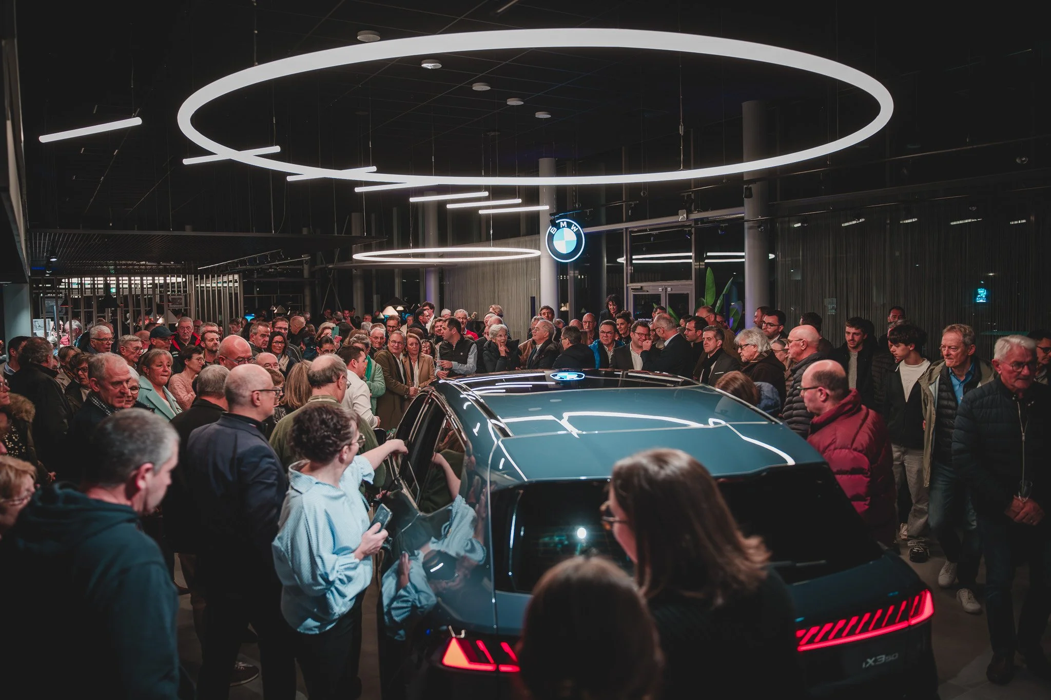 Présentation d'une voiture dans un showroom BMW, entourée d'une foule lors d'un événement.