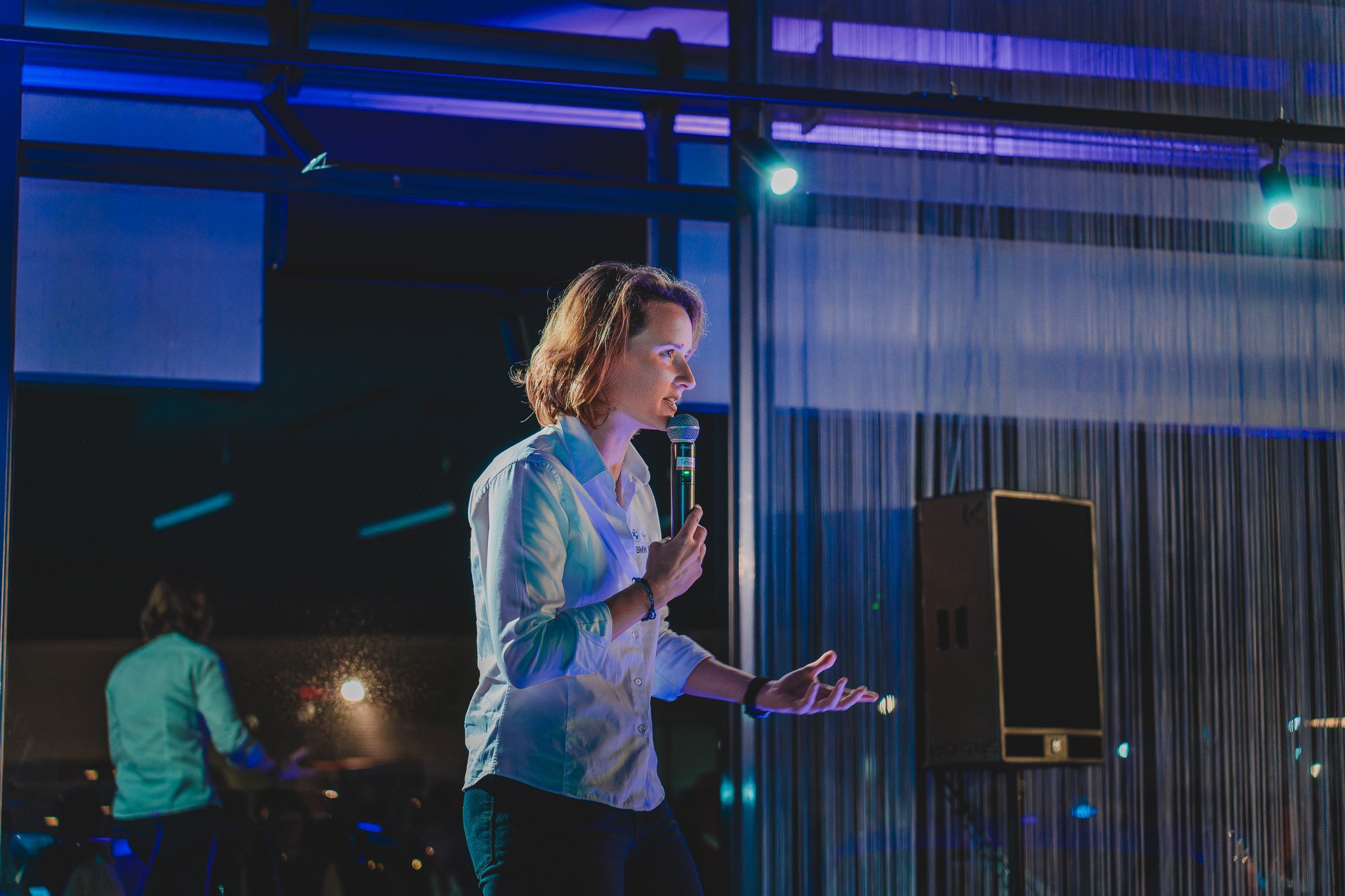 Femme parlant dans un micro lors d'un événement avec éclairage coloré et décor moderne.
