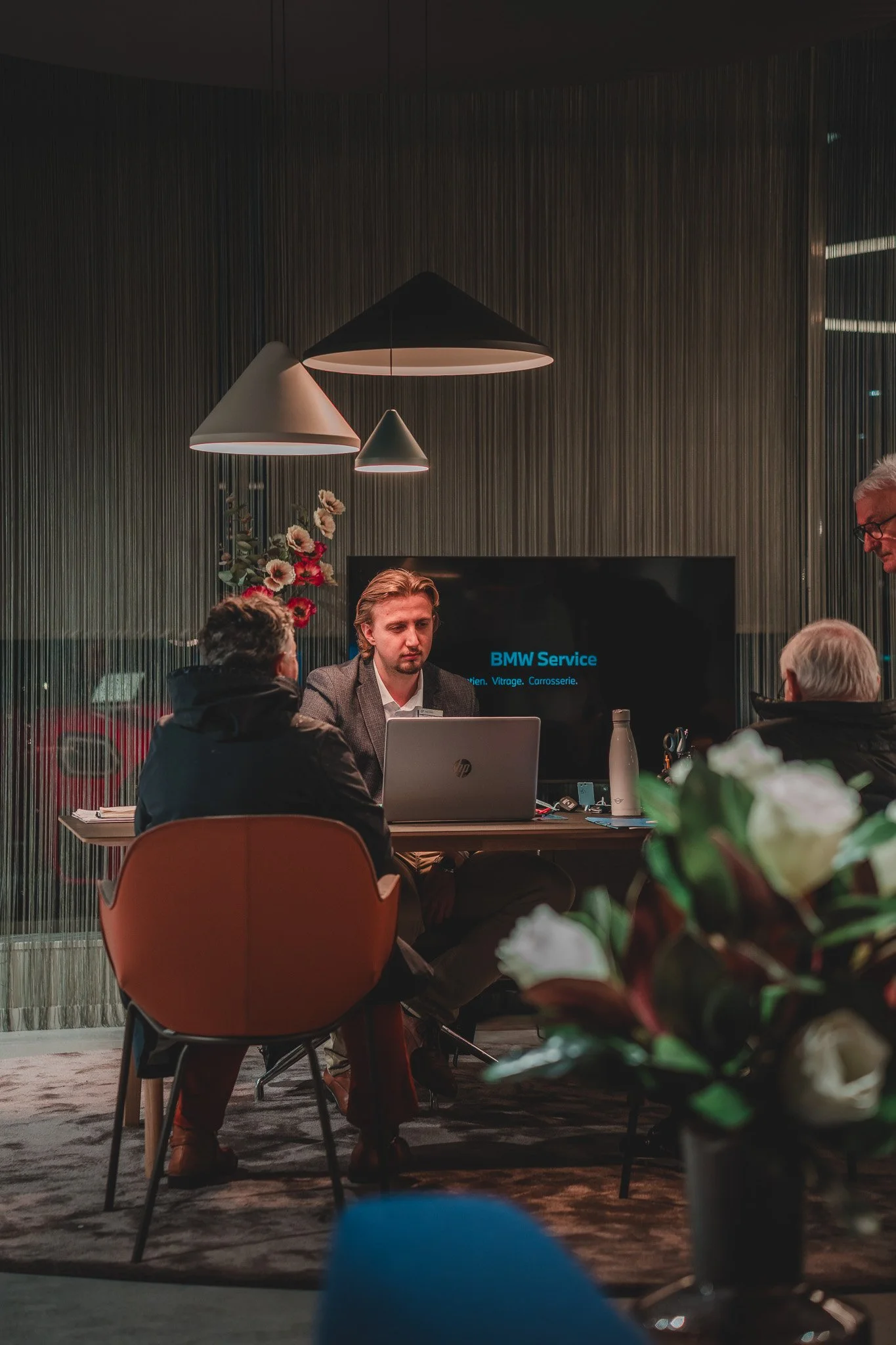 Consultation automobile en intérieur, avec un vendeur ou mécanicien expliquant un service BMW à un client, dans un espace moderne et élégant