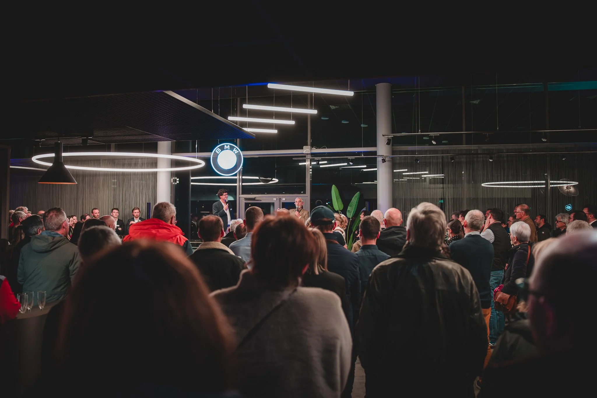 Une assemblée de personnes dans une salle moderne, assistent à une conférence ou un événement, avec le logo BMW visible en arrière-plan.