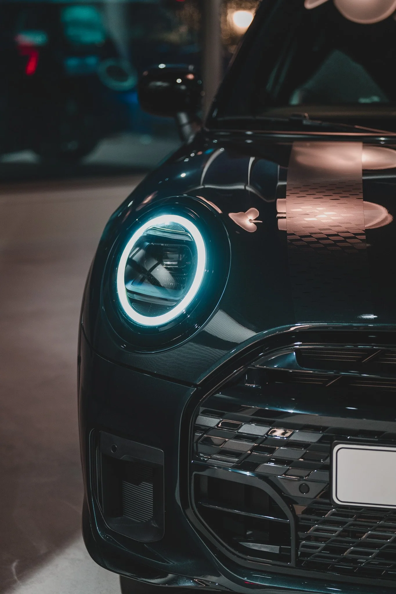 Première vue rapprochée du devant d'une voiture noire avec un phare à LED allumé, dans un environnement nocturne.