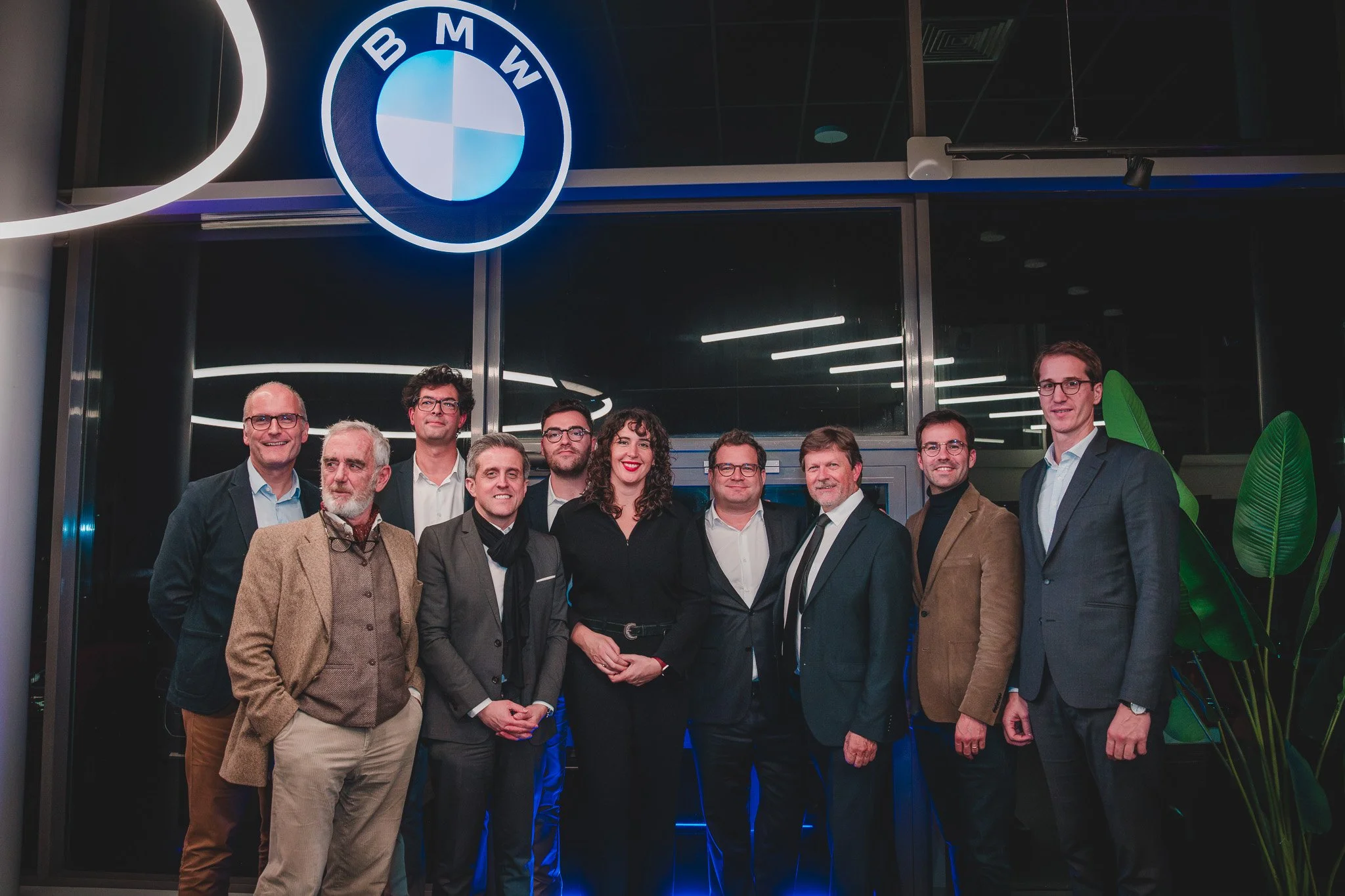 Groupe de dix personnes habillées en costume posant devant un logo BMW illuminé dans un bâtiment moderne.