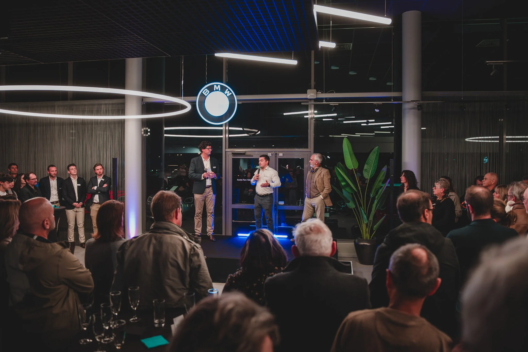 Cérémonie de remise de prix ou discours dans une salle d'exposition avec un logo BMW sur la vitre.