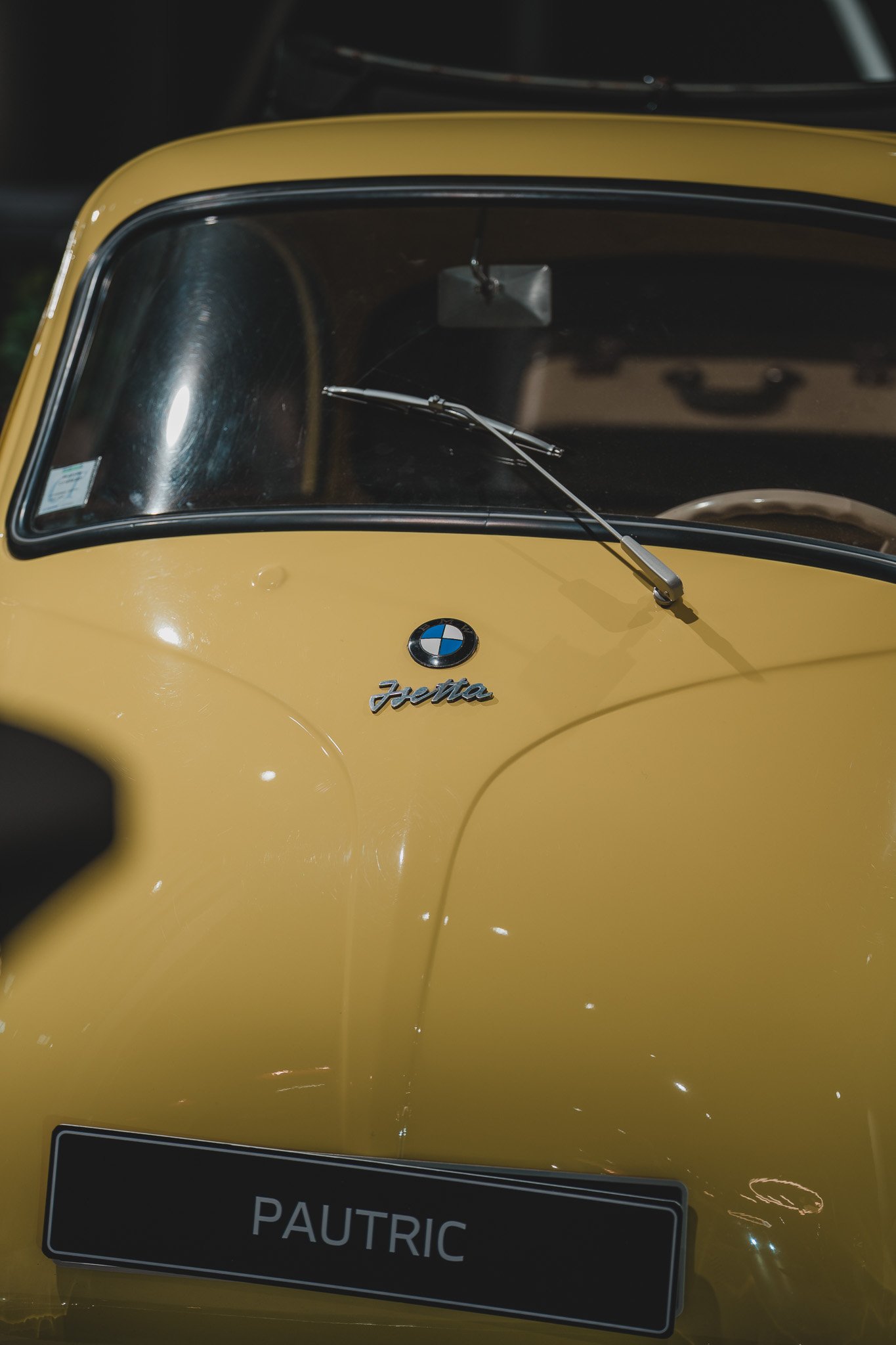 Une voiture jaune vintage avec le logo BMW et la plaque d'immatriculation 'PAUTRIC'.
