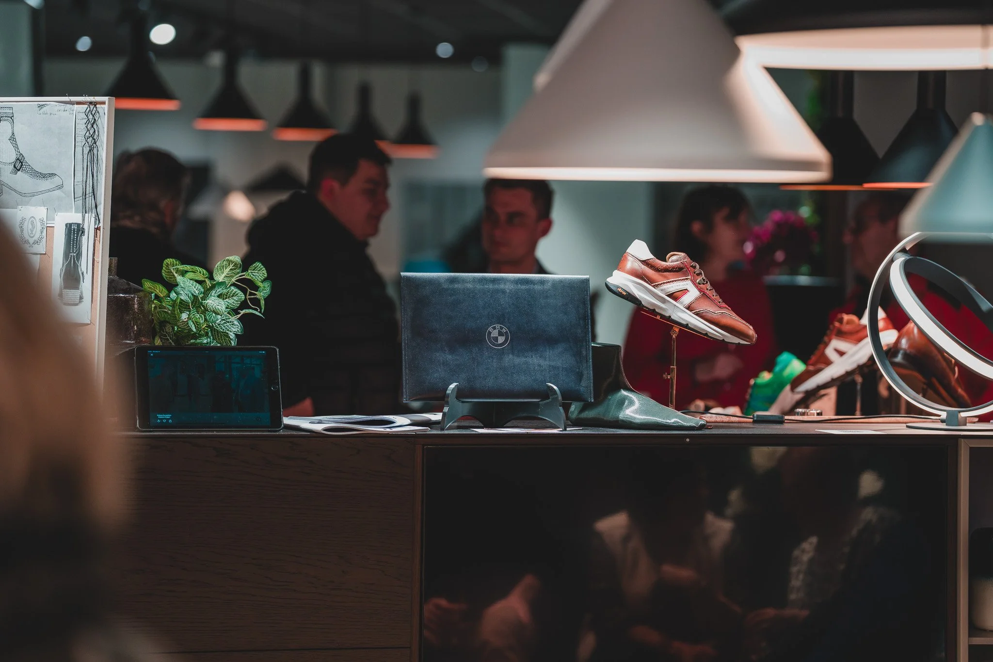 Vitrine de chaussures de sport en vente dans un magasin, avec des lumières suspendues au plafond et plusieurs personnes en arrière-plan.