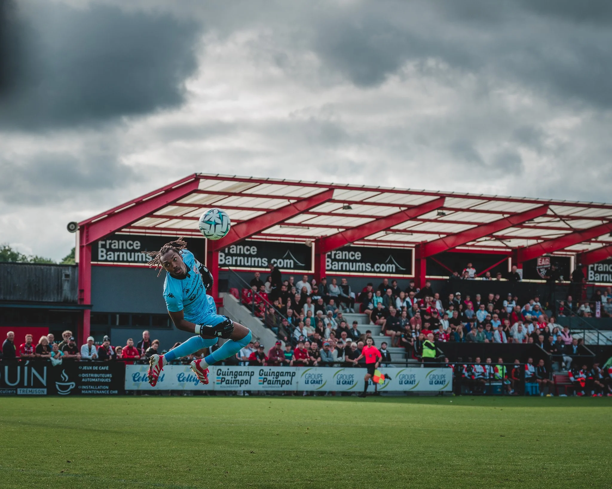 Un joueur de football en train de sauter pour toucher le ballon, avec un public en arrière-plan dans un stade.