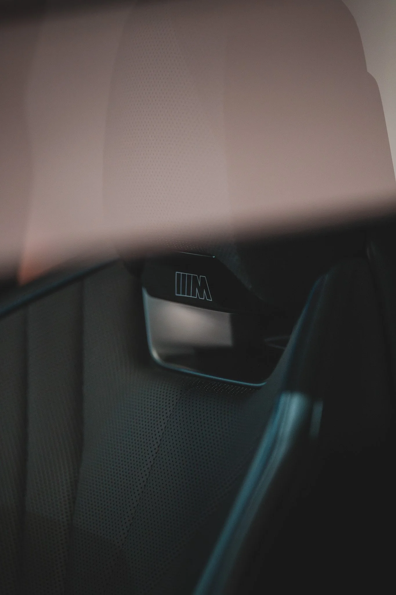 Intérieur d'une voiture, vue d'une poignée de porte avec le logo BMW M en noir et blanc, et un siège en cuir perforé.