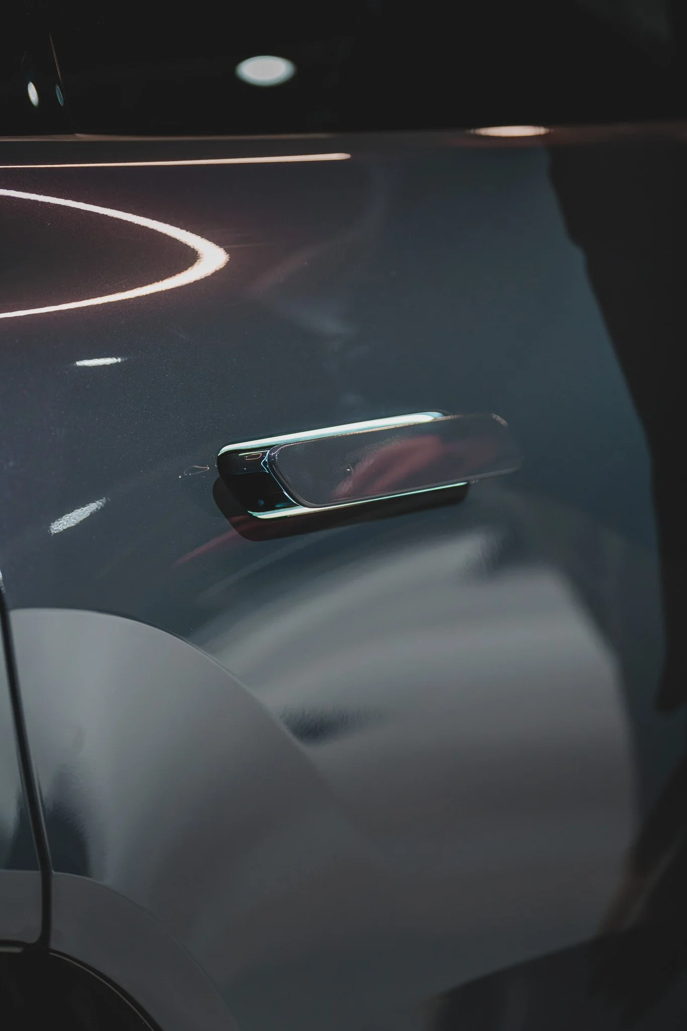 Prise de vue proche d'une poignée de porte de voiture noire avec reflexions lumineuses.