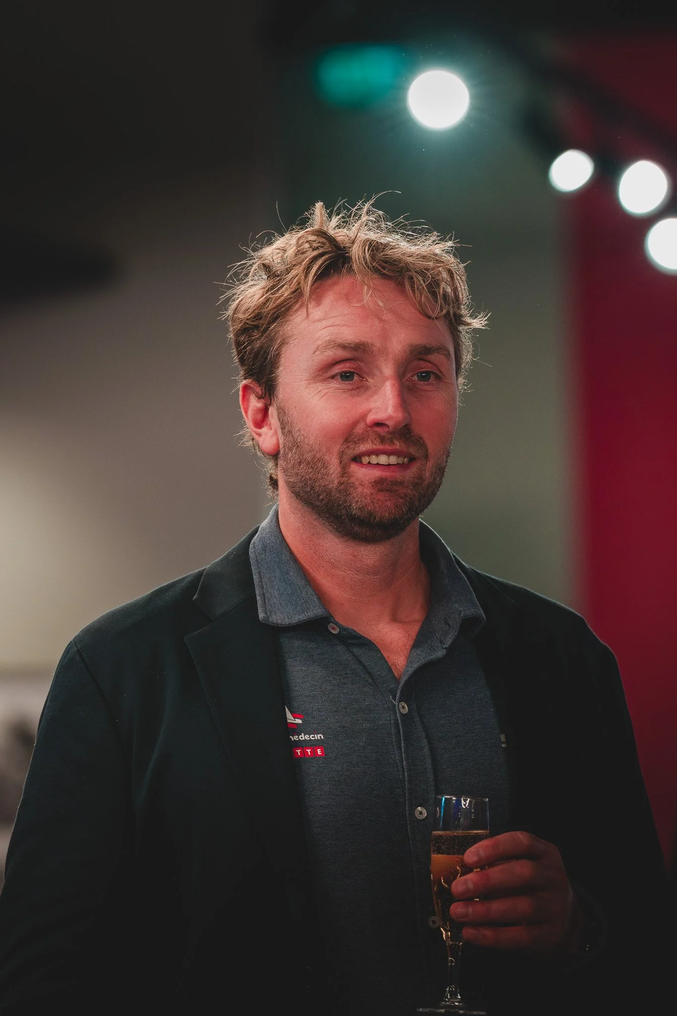 Homme avec une barbe, en train de trinquer avec une flûte de champagne à une fête ou un événement social.