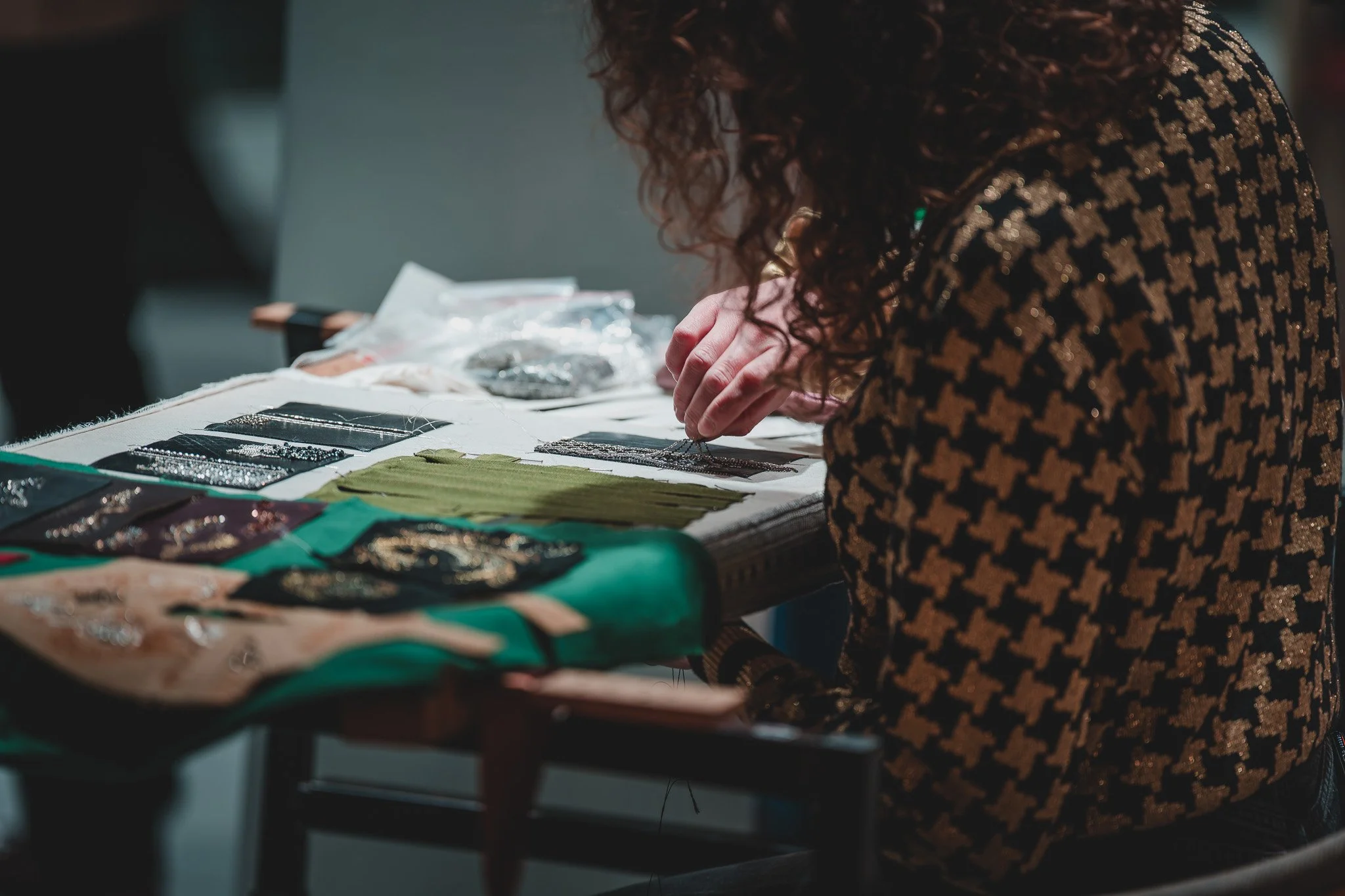 Personne cousant des détails en perles ou broderies sur un tissu lors d'un atelier ou d'une démonstration.