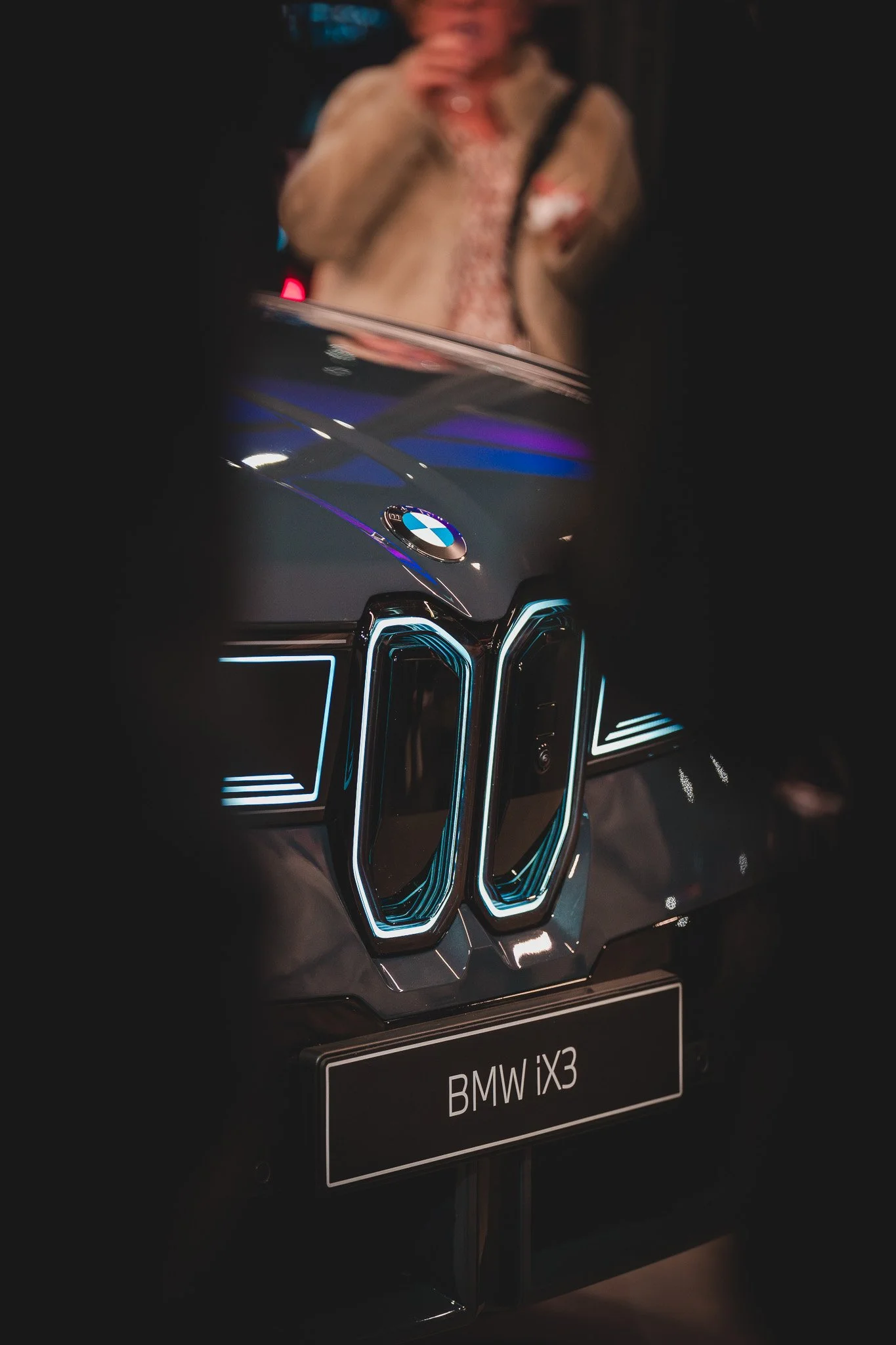 Une présentation d'une voiture BMW iX3, avec le logo BMW visible sur le capot et un panneau indiquant le modèle.