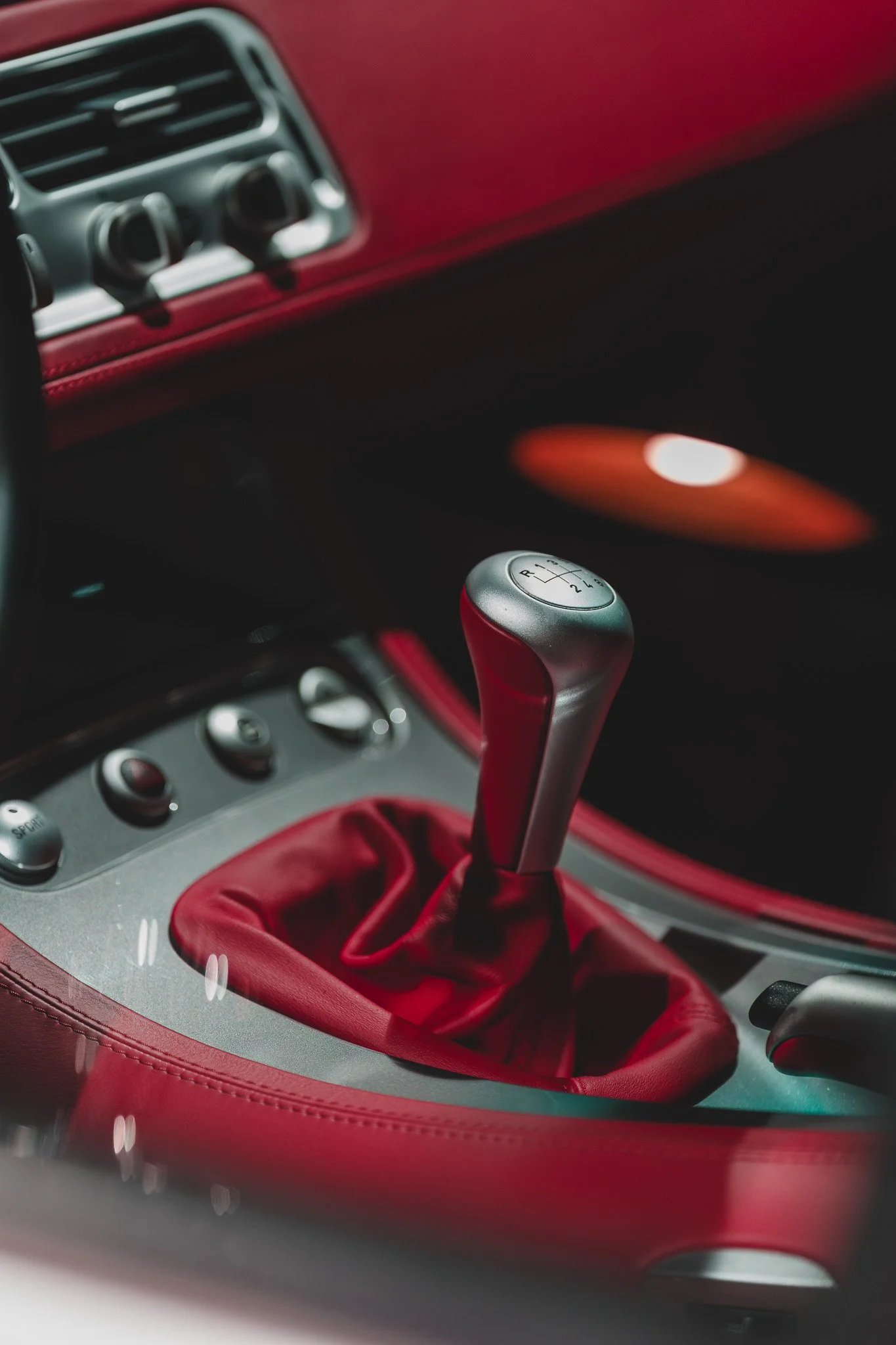 Intérieur de voiture avec levier de vitesse en métal, boutons de contrôle et garniture rouge.
