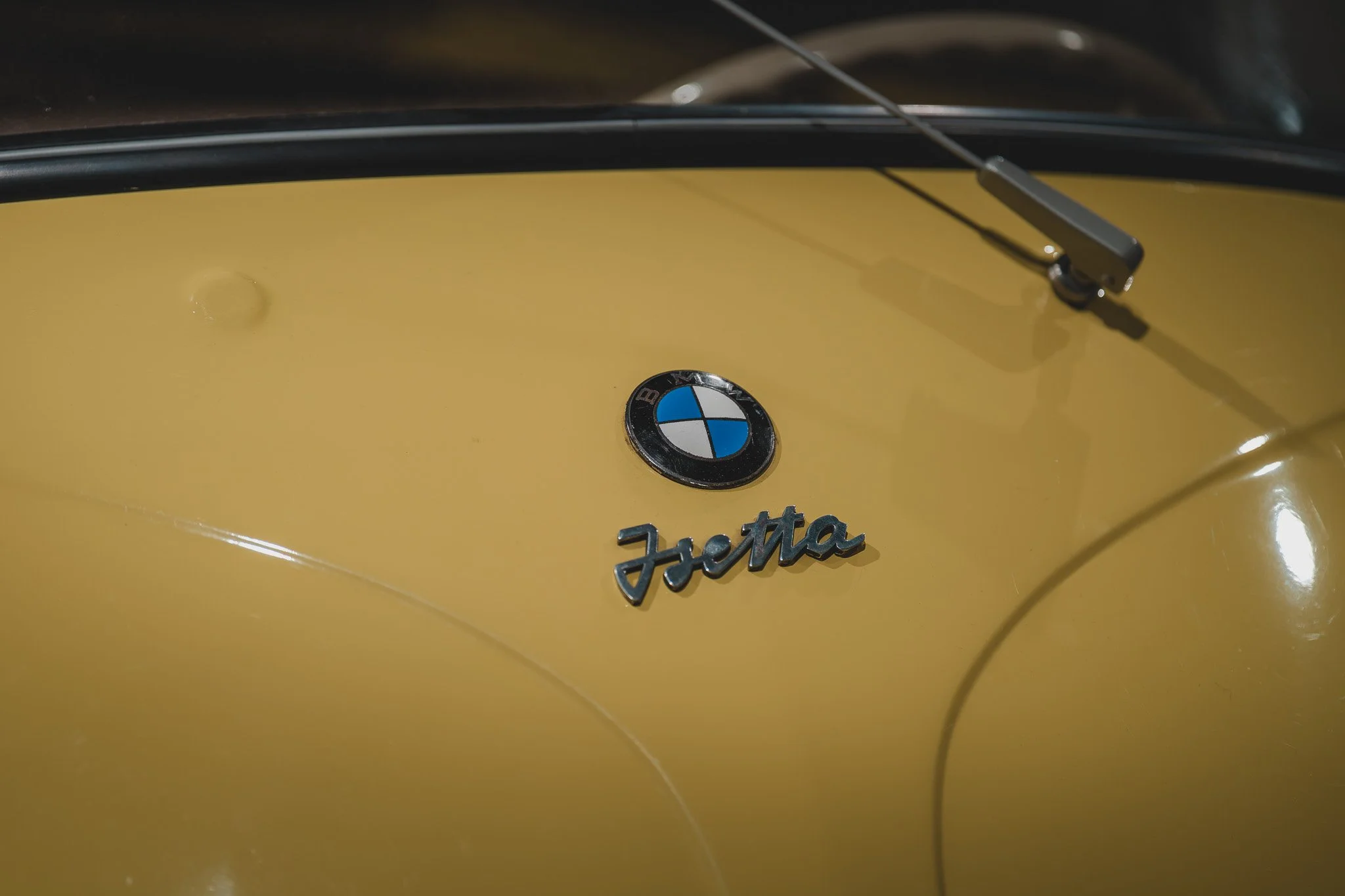 Un logo BMW et une inscription Fetta sur le capot d'une voiture jaune classique.