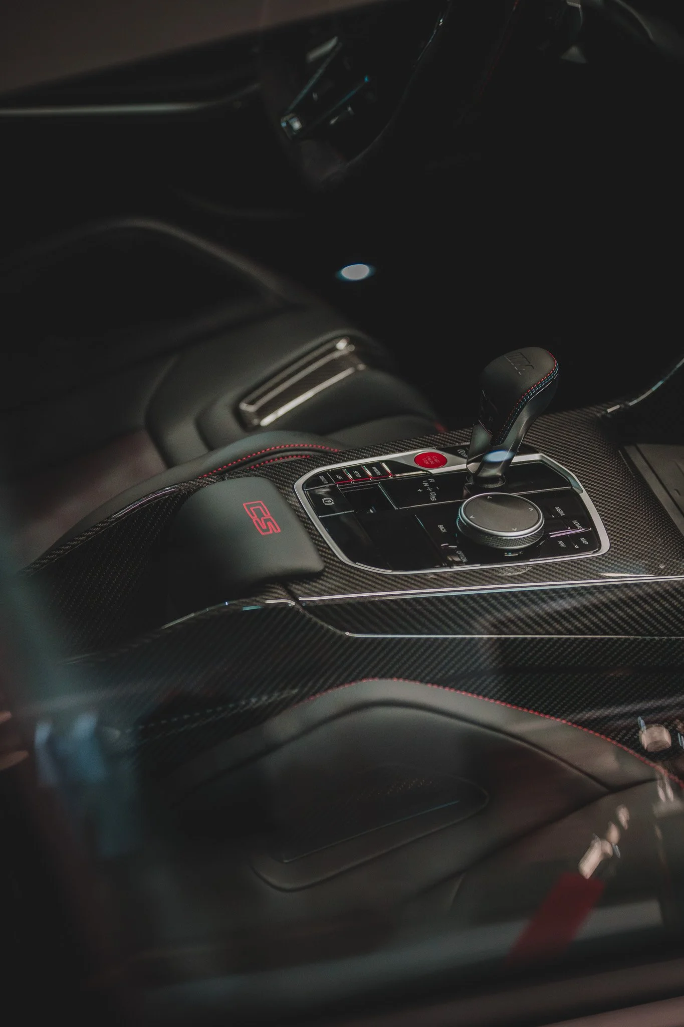 Intérieur d'une voiture de luxe avec un centre de console en fibre de carbone, un levier de changement de vitesse, un bouton rouge, et un logo 'RS' en rouge.