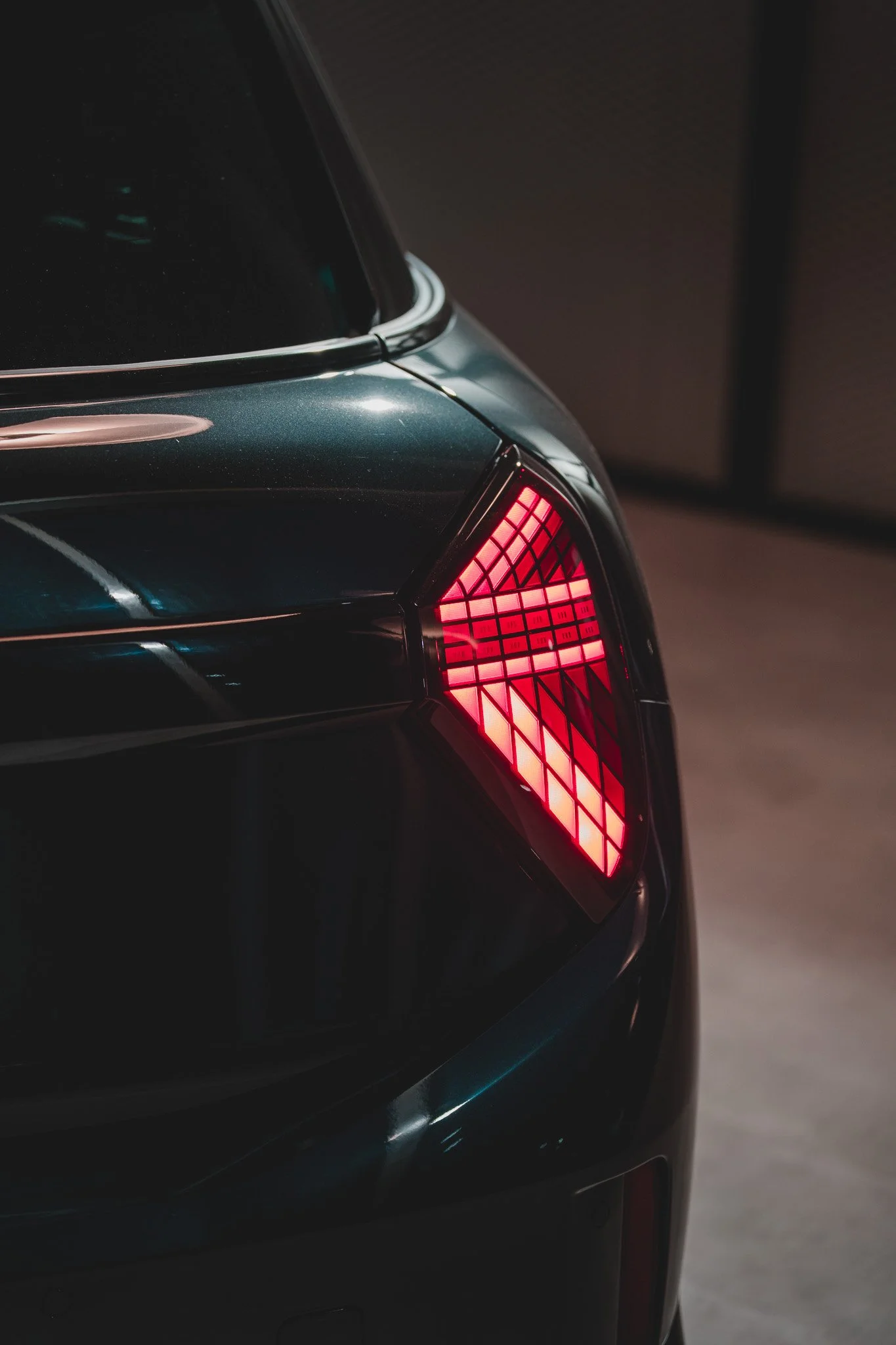 Fermeture des feux arrière d'une voiture de sport noire dans une pièce sombre.