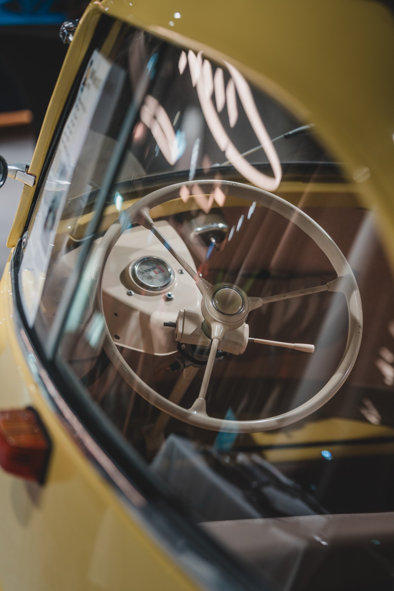 Jeu de lumière sur un tableau de bord vintage d'une voiture jaune, vue à travers une vitre qui crée des reflets.