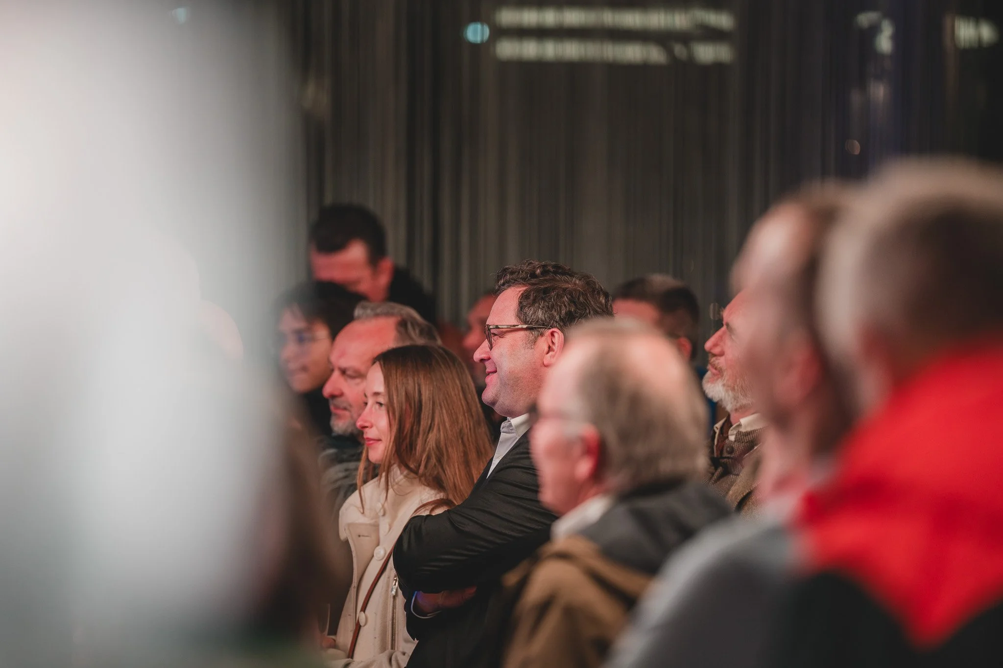 Groupe de personnes assises en auditorium, assistant à une présentation ou un événement, souriant et attentif.