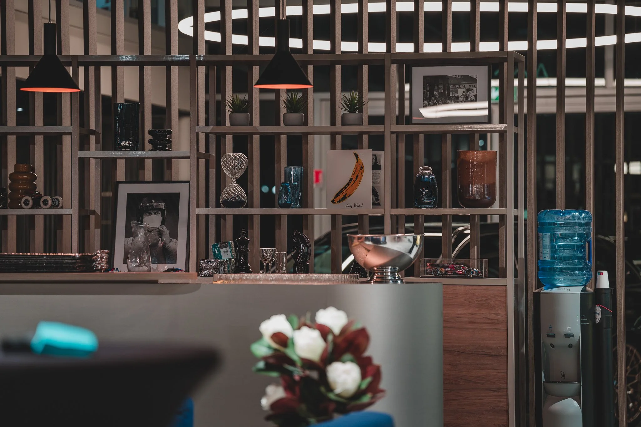Vitrine d'une boutique avec des éléments décoratifs, des plantes en pot, des cadres photo, des objets en verre et une bouteille d'eau bleue.