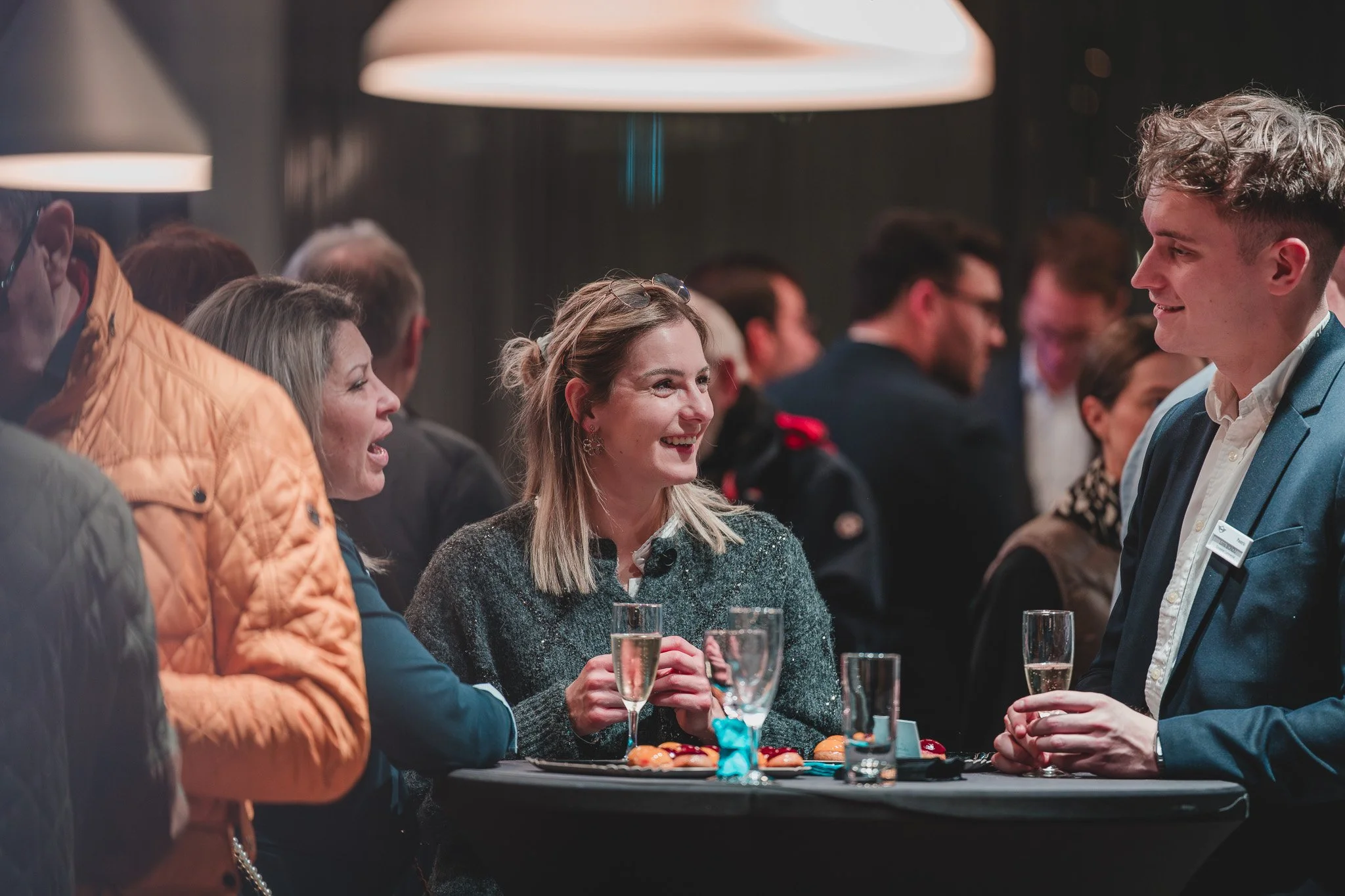Groupe de personnes discutant et souriant lors d'une réception, avec des boissons et des amuse-bouches sur la table.