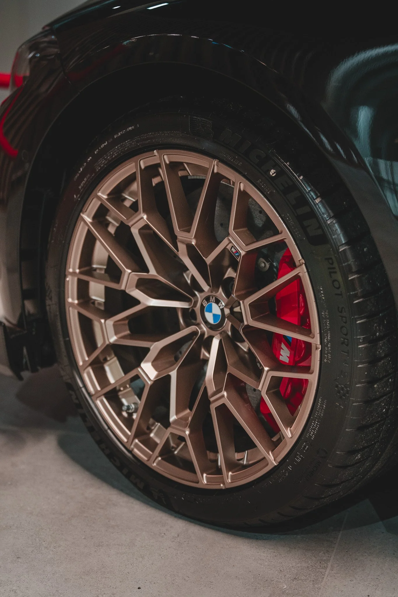 Roue de voiture BMW avec jante en alliage dorée, frein à disque rouge et pneu Michelin Pilot Sport.