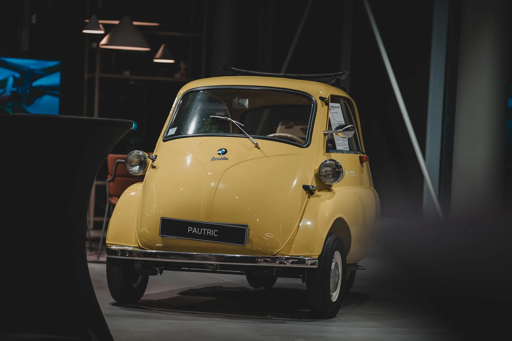 Une petite voiture jaune appelée Pautric exposée dans un musée, dans un environnement avec un éclairage tamisé.