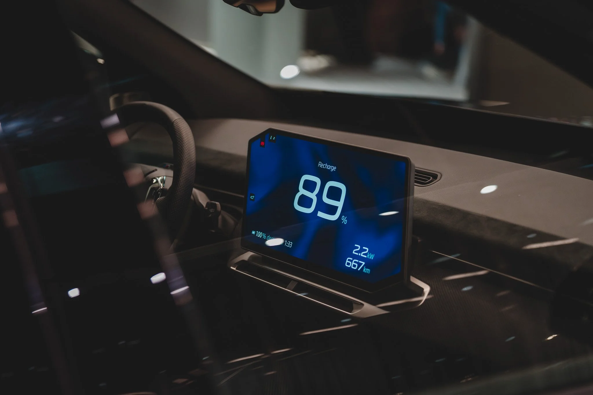 Tableau de bord intérieur d'une voiture électrique affichant une recharge à 89%, une autonomie de 667 km, et une puissance de 2,2 kW.