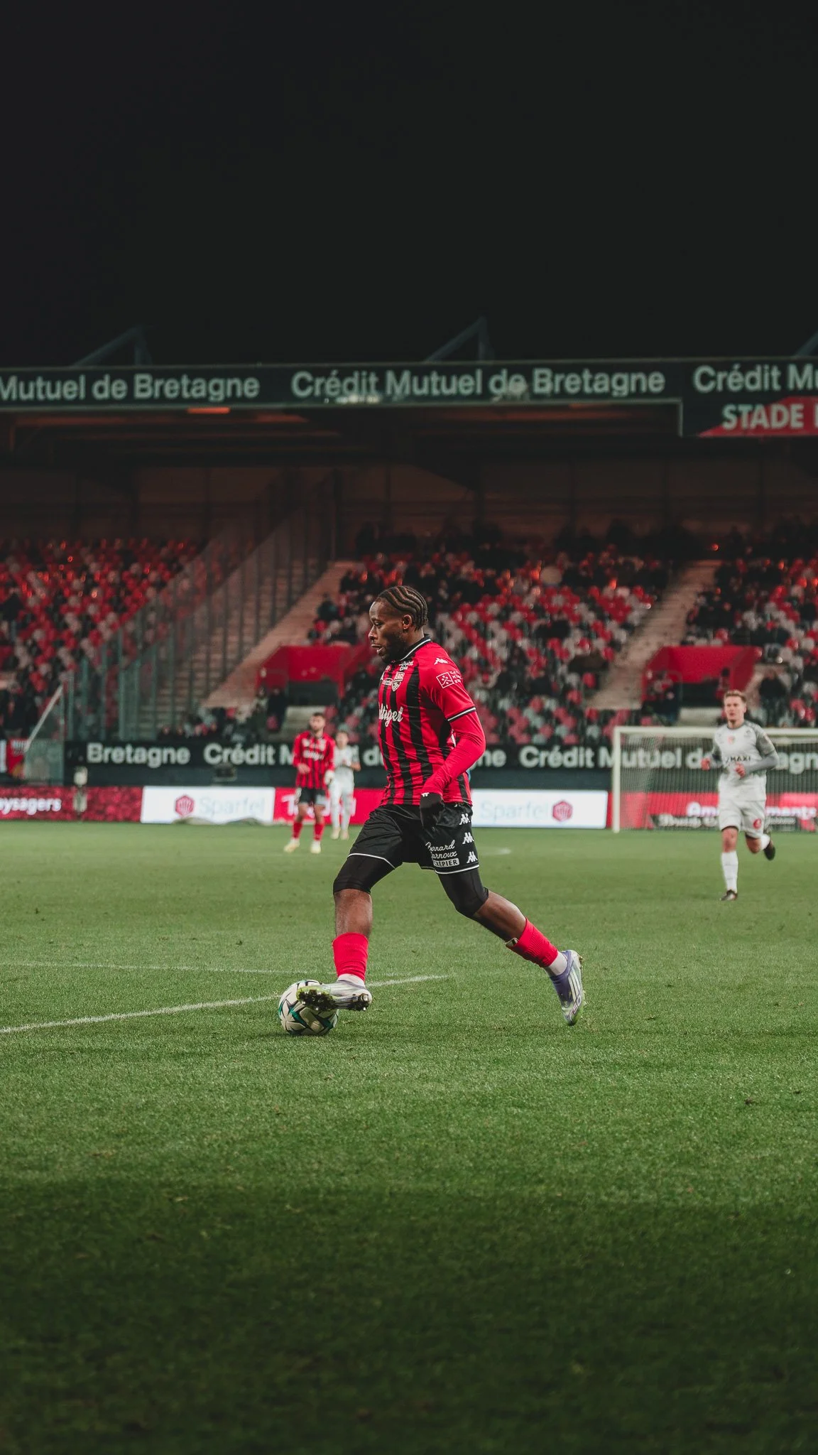 Un joueur de football portant un maillot rayé rouge et noir, en train de jouer sur le terrain d'un stade lors d'un match