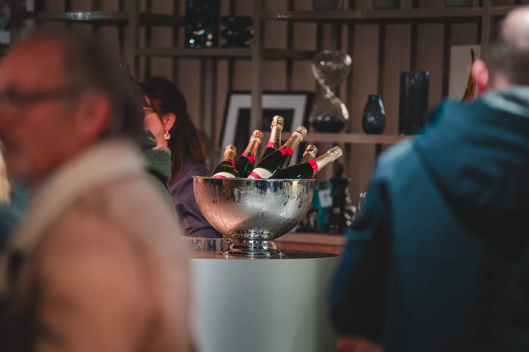 Verre d'argent rempli de bouteilles de champagne dans un bar, entouré de personnes.
