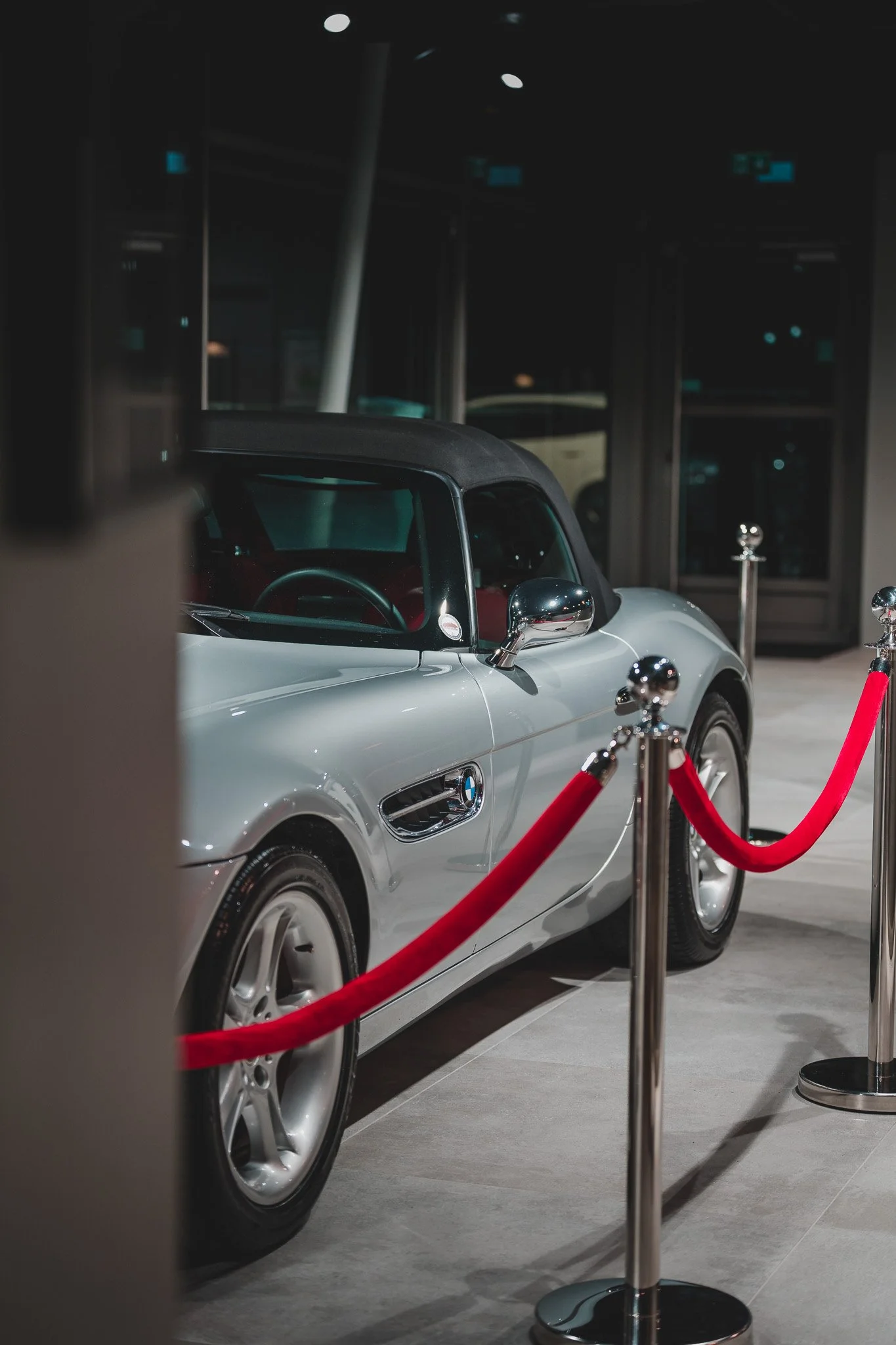 Voiture de luxe BMW exposée dans une galerie, entourée de cordons rouges et de barres de séparation, dans un contexte d'exposition ou de musée.
