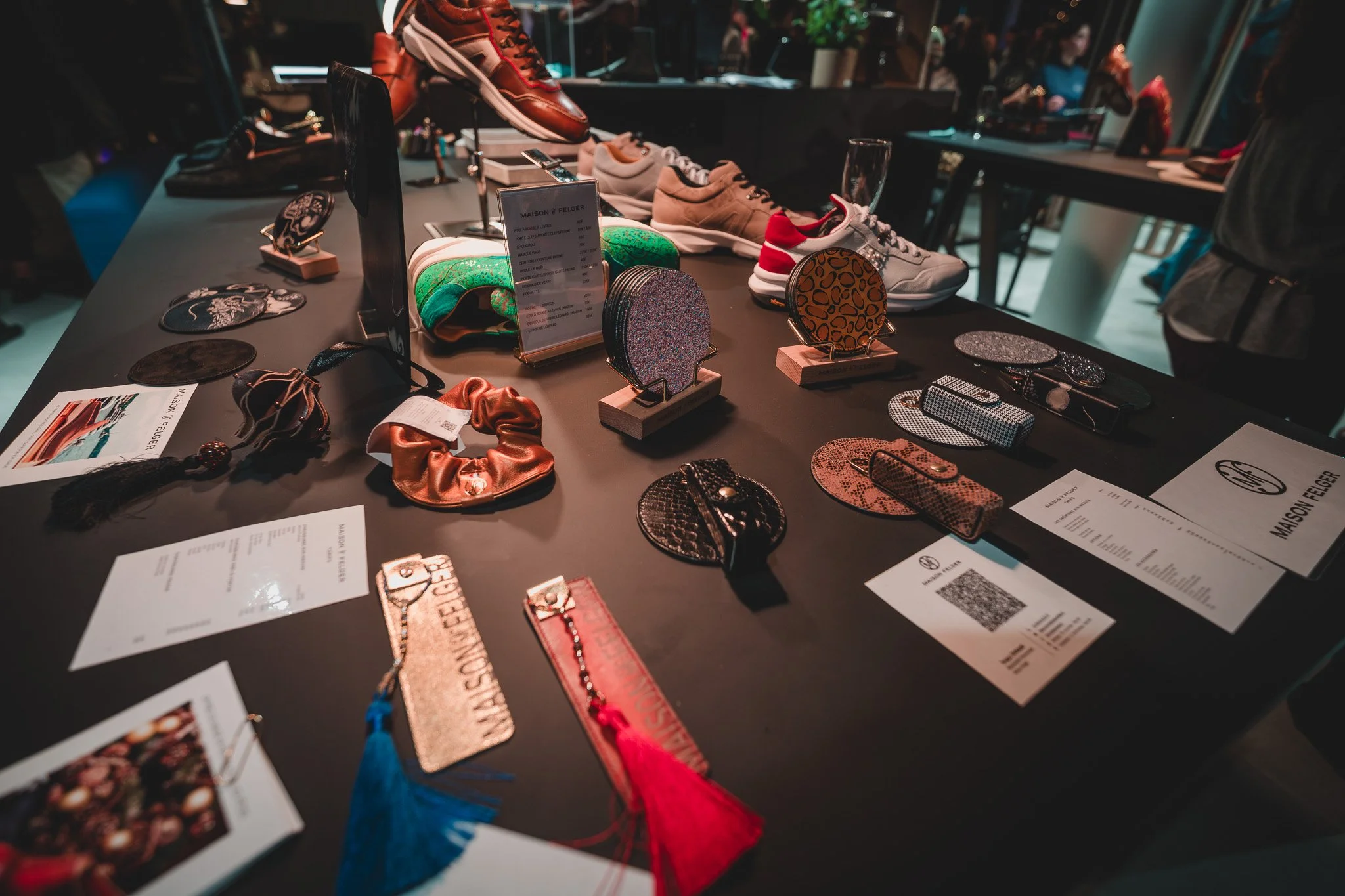 Une table d'exposition de chaussures, sacs et accessoires de mode, avec des sneakers, des sacs à main, des bijoux, des porte-clés, et des éléments décoratifs, dans une boutique ou lors d'un événement de mode.