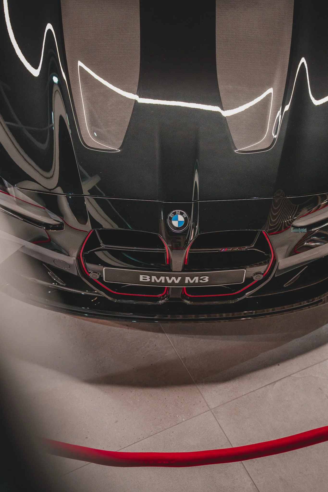 Vue de face d'une voiture noire BMW M3 avec un logo BMW et une calandre distinctive, affichant une plaque avec l'inscription "BMW M3".