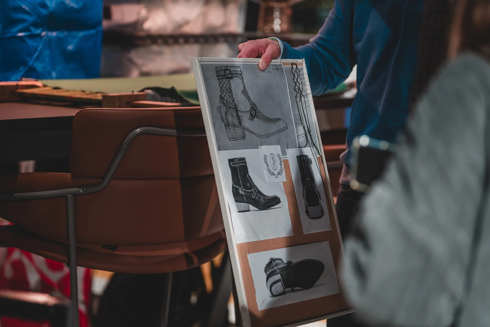 C'est une image d'une personne montrant un tableau d'idées pour des chaussures, avec des dessins techniques et des photos de bottes en cuir noires.