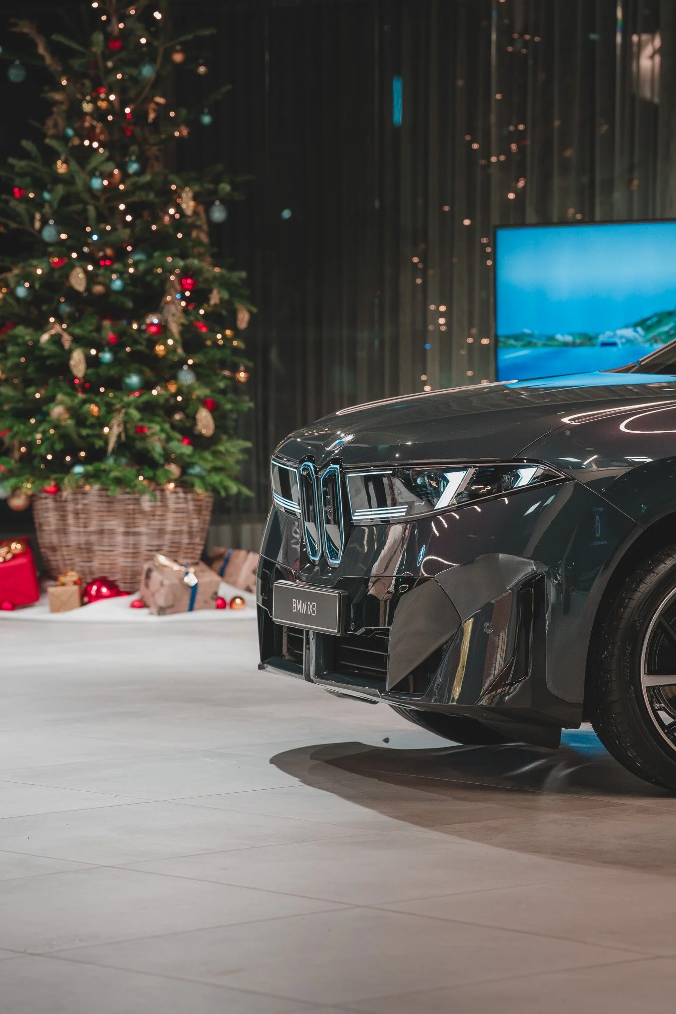 Voiture BMW X3 noire devant un sapin de Noël décoré, avec des cadeaux en arrière-plan.
