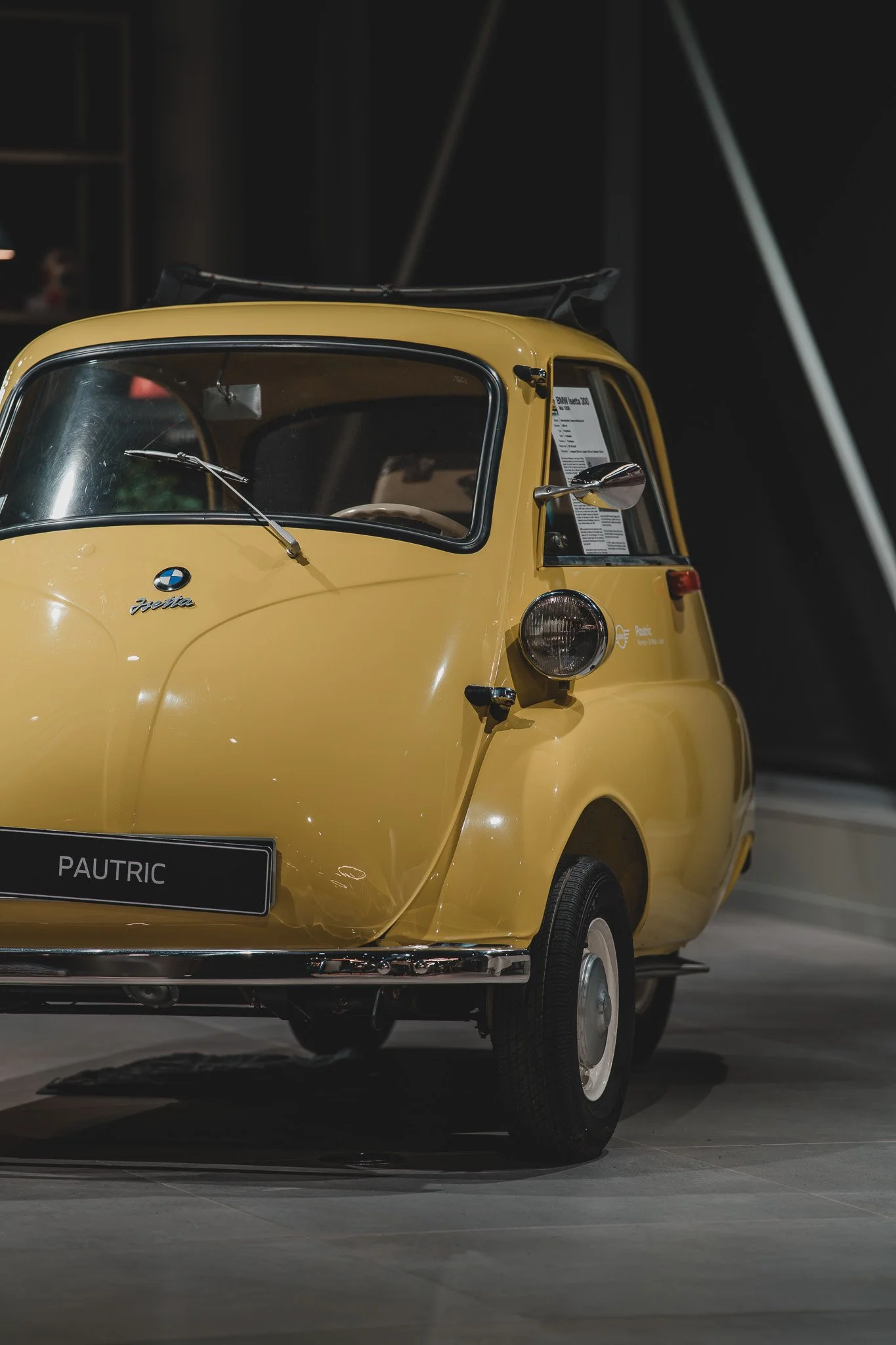 Une petite voiture jaune, modèle BMW Isetta, exposée dans un musée, avec un insignifiant logo BMW et la plaque d'identification PAUTRIC.
