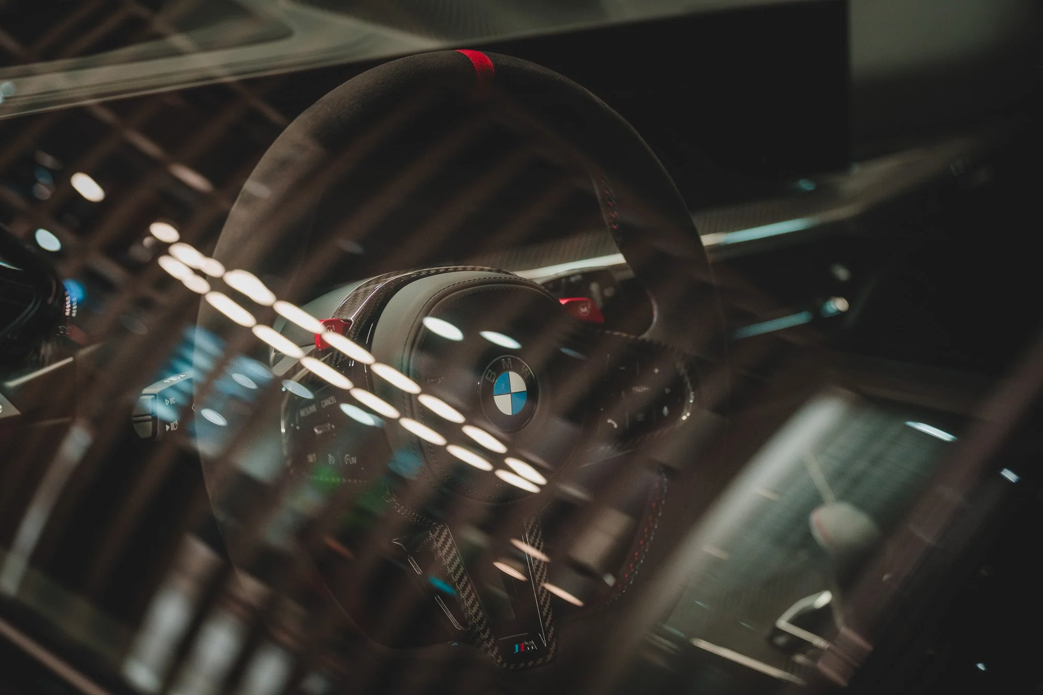 Intérieur d'une voiture de sport BMW, vue du cockpit avec volant en cuir, boutons, et instrumentation, prise en photo à travers une grille ou un écran de protection.