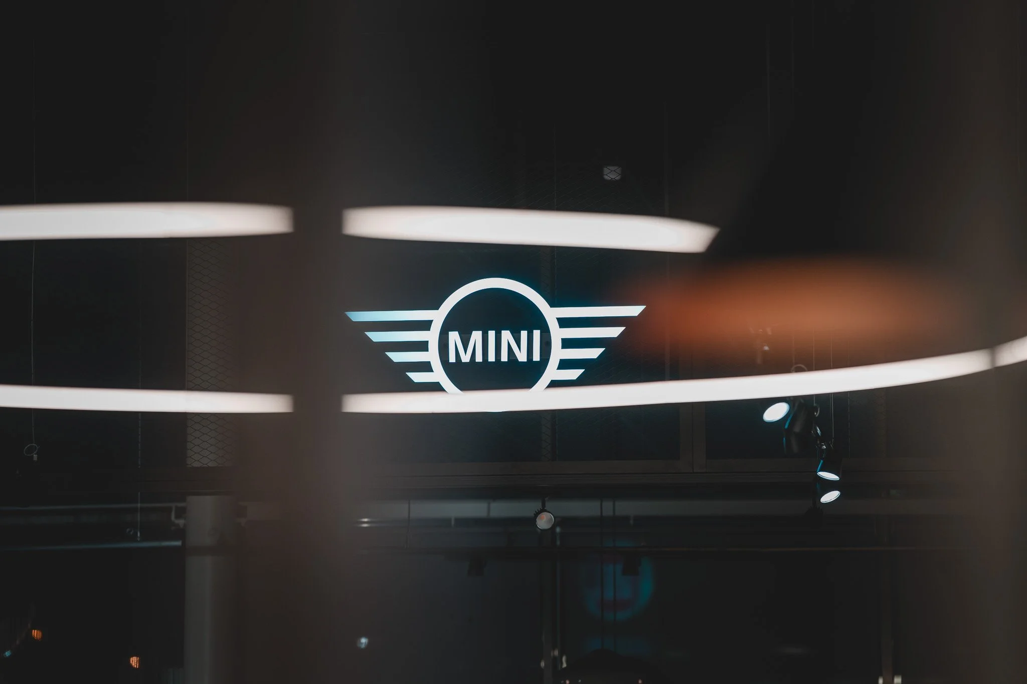 Logo de la marque Mini, représentant un cercle avec les ailes de chaque côté, sur un fond sombre, avec un éclairage de spots