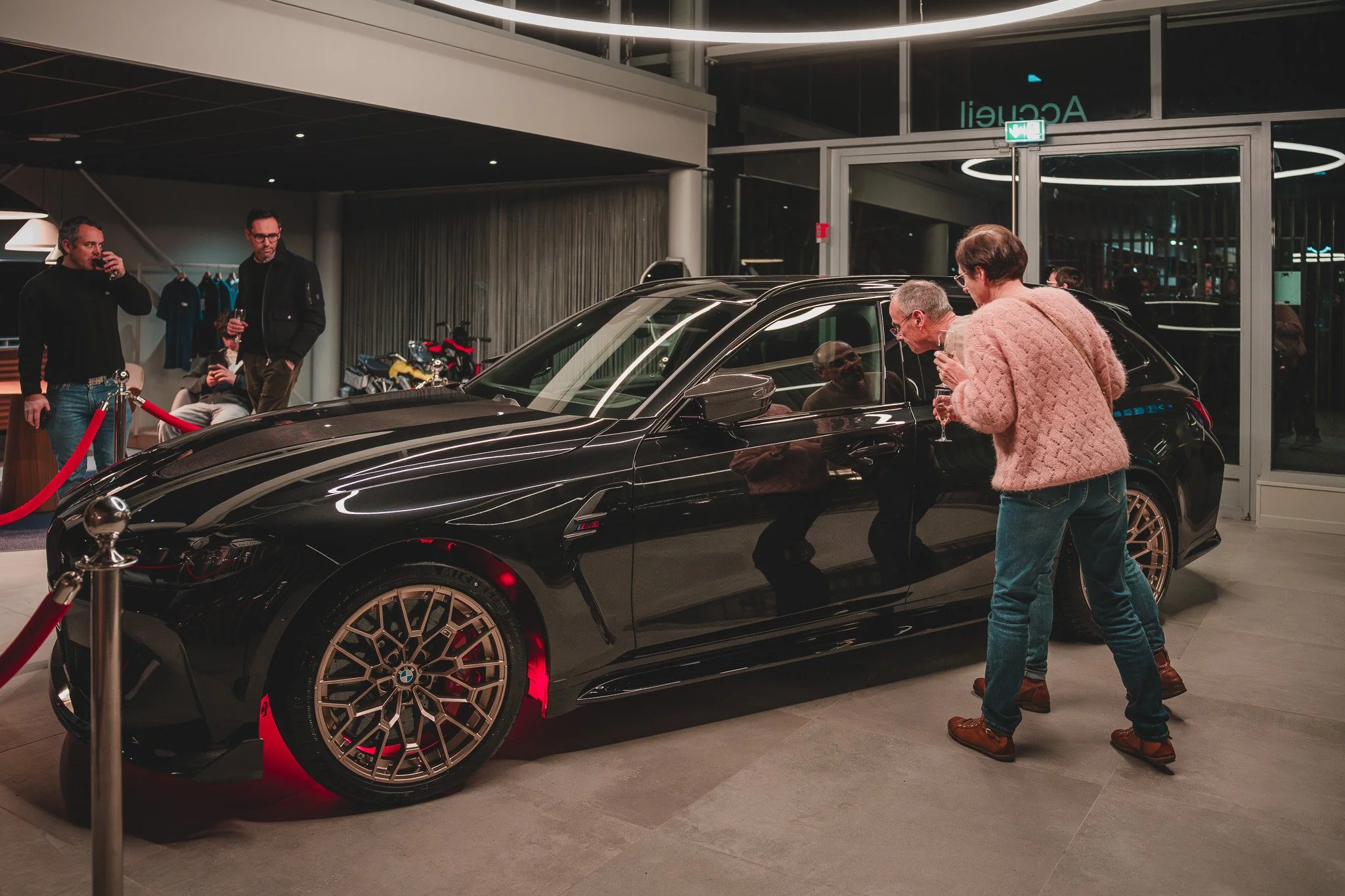 Groupe de personnes admirant une voiture noire de luxe dans un showroom.