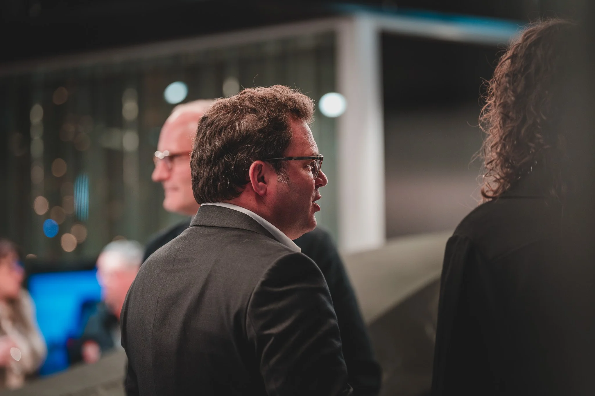 Trois personnes discutant lors d'une réunion ou d'une conférence, vues en profil, dans un environnement professionnel