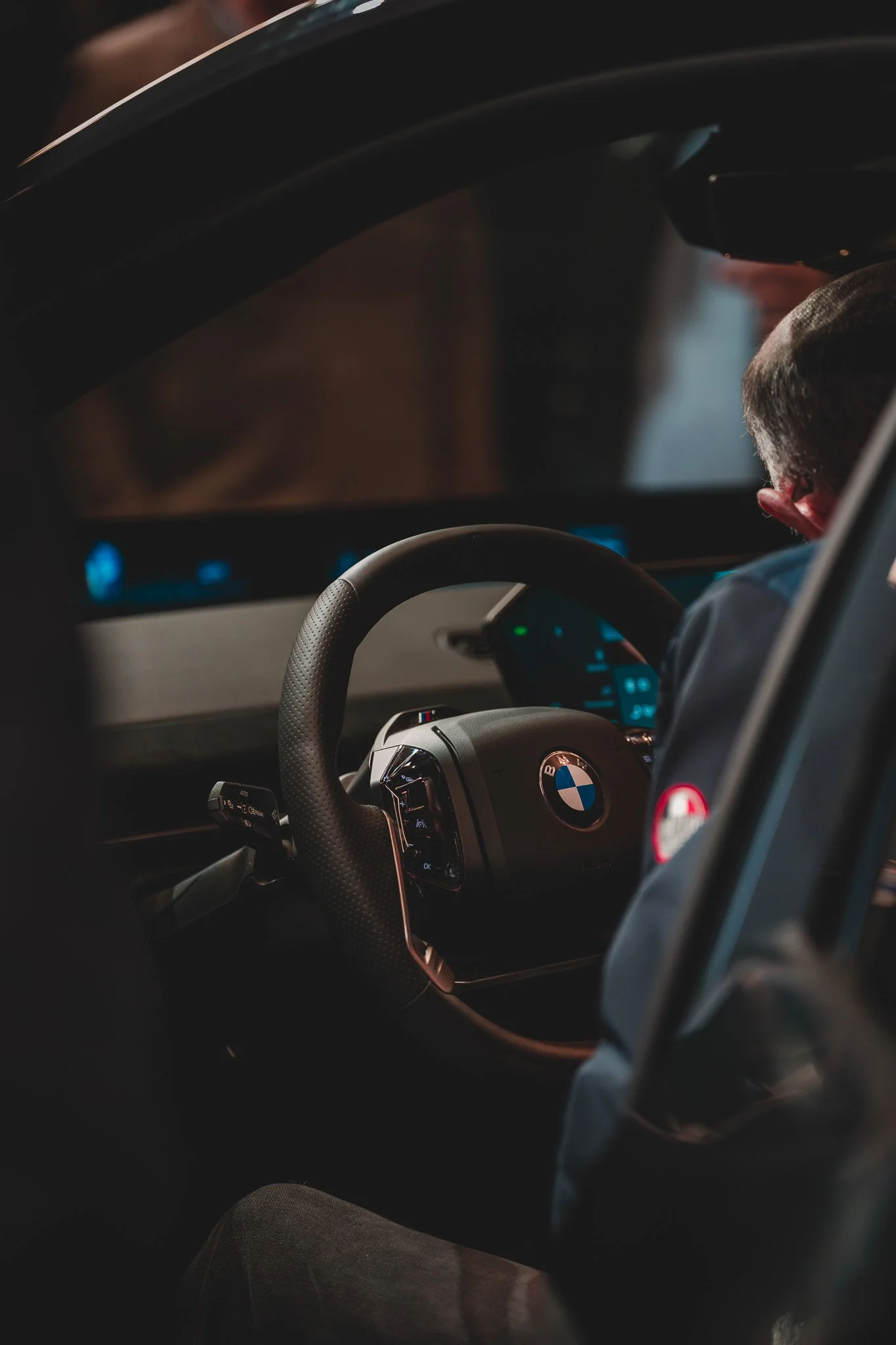 Intérieur d'une voiture BMW, vue du tableau de bord et du volant, avec une personne dans le siège conducteur, en arrière-plan.