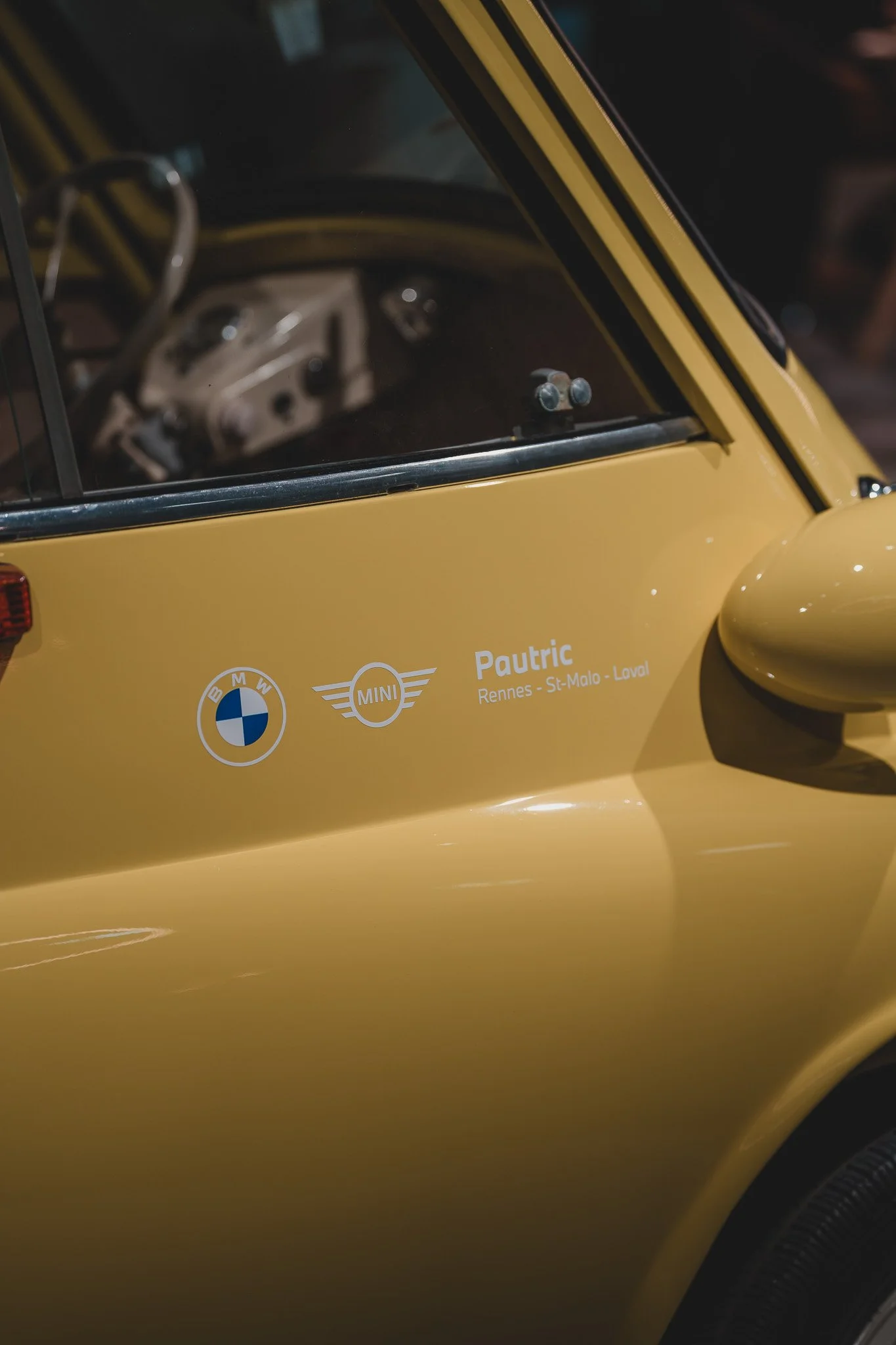 Photo d'une voiture jaune miniature avec les logos BMW et MINI, et le texte 'Pautric Rennes - St-Malo - Loval'.