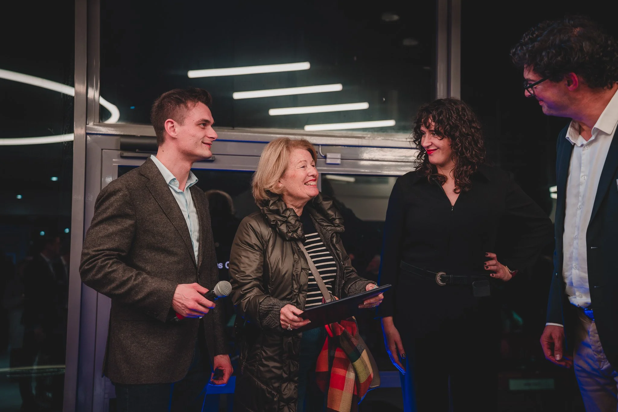 Quatre personnes discutent et sourient lors d'une rencontre en intérieur, probablement dans un cadre professionnel ou social.