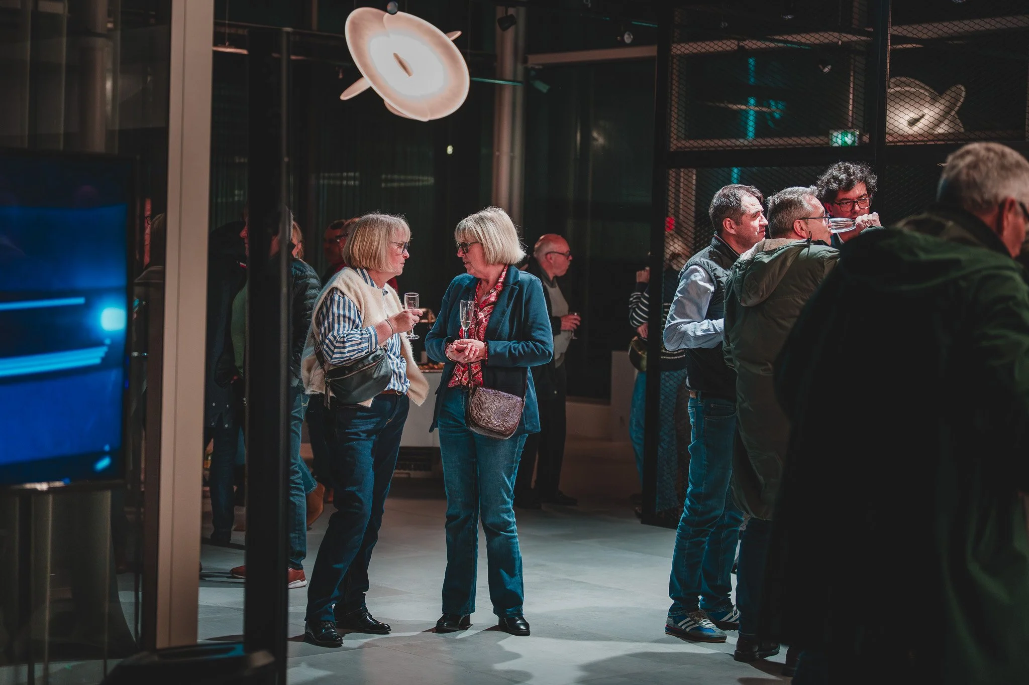 Groupe de personnes à une exposition ou un événement, discutant et buvant des boissons dans un espace intérieur moderne.