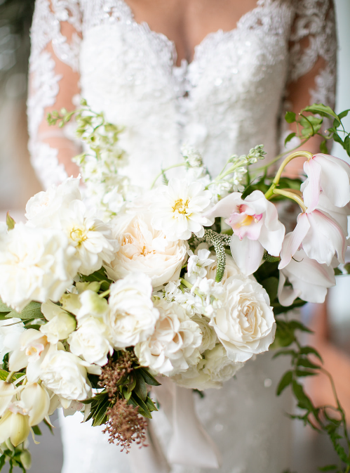 Bride holding a bouquet of white and blush flowers in front of her lace wedding dress.