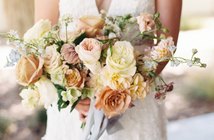 Person holding a bouquet of pastel-colored roses and peonies.