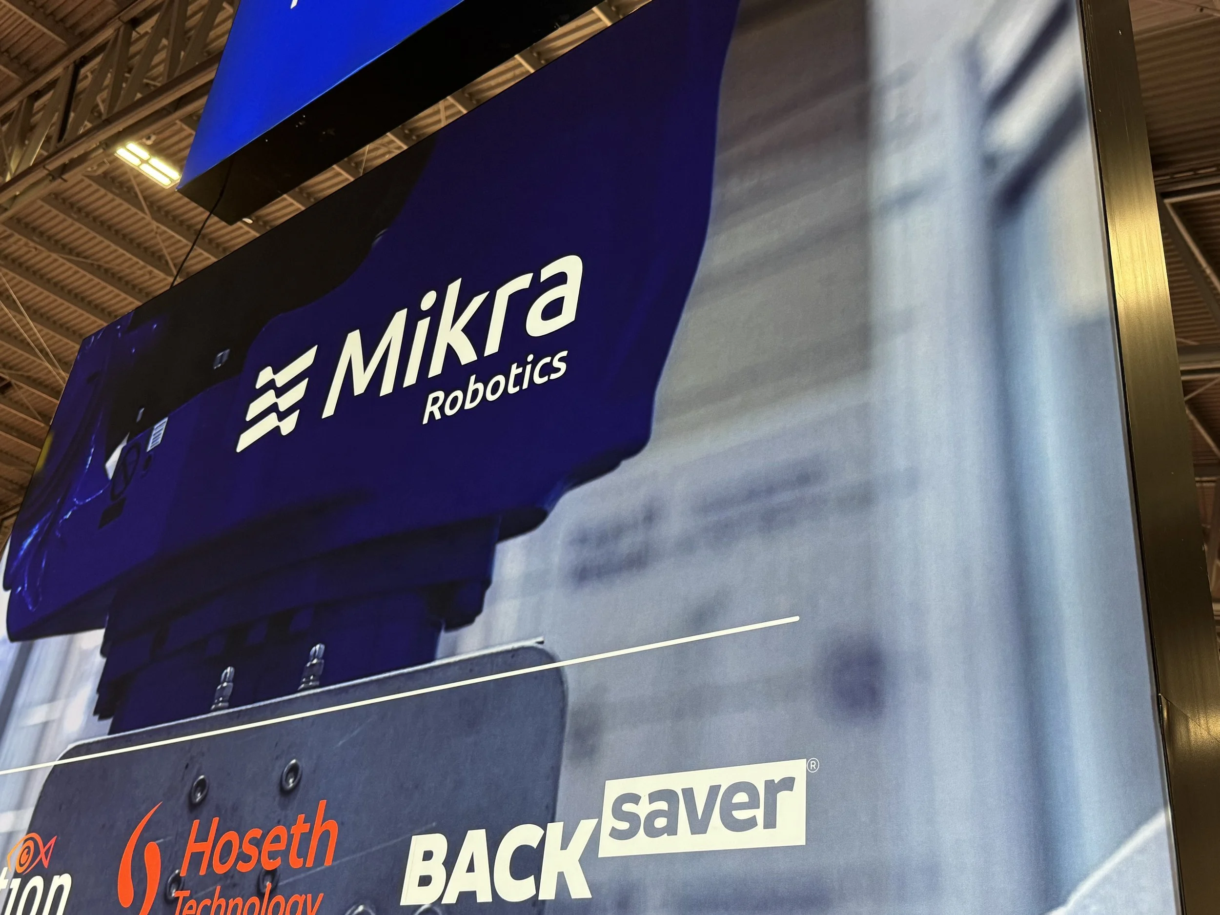 Heildarmynd af sýningarbás Mikra með bláum og hvítum merkingum, skjám og upphengdum skiltum.