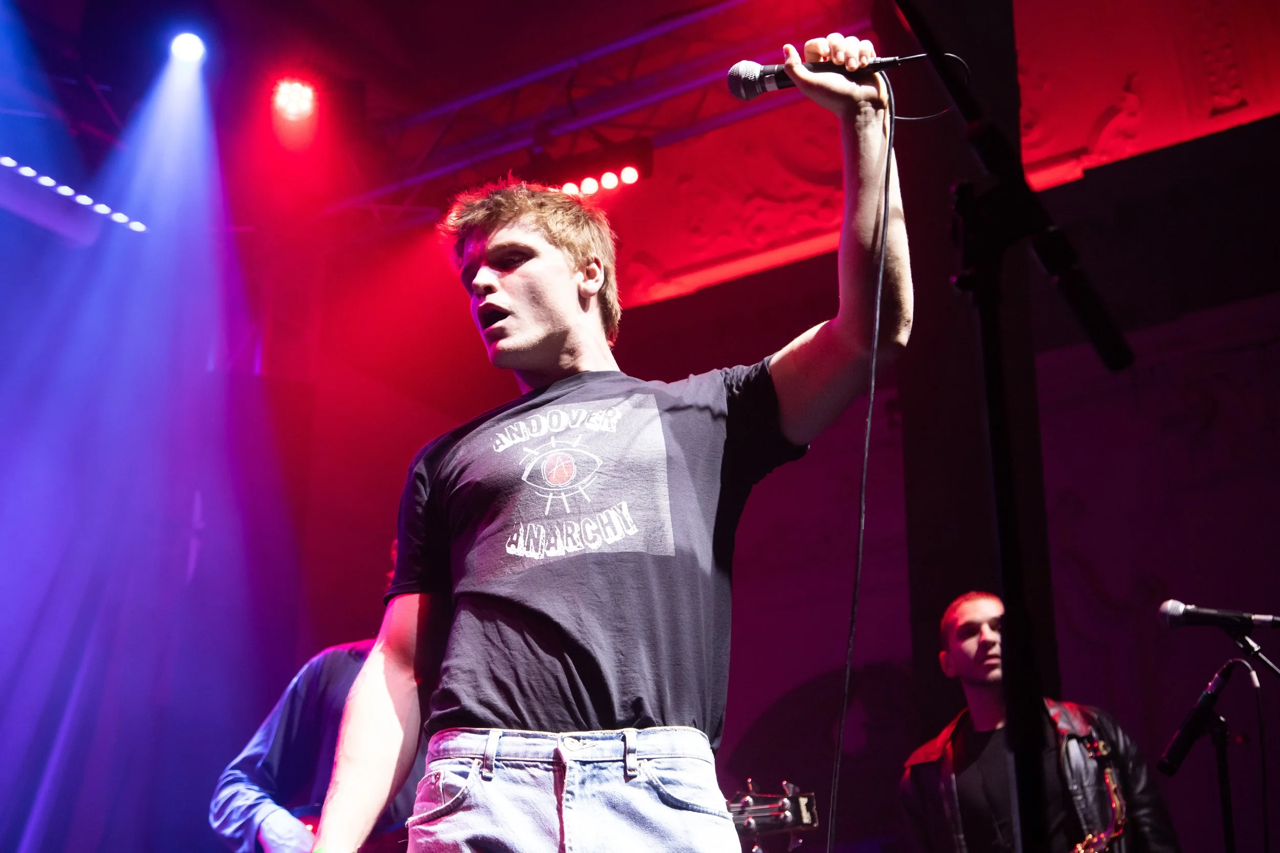A person holding a microphone on stage under colorful lights during a concert.