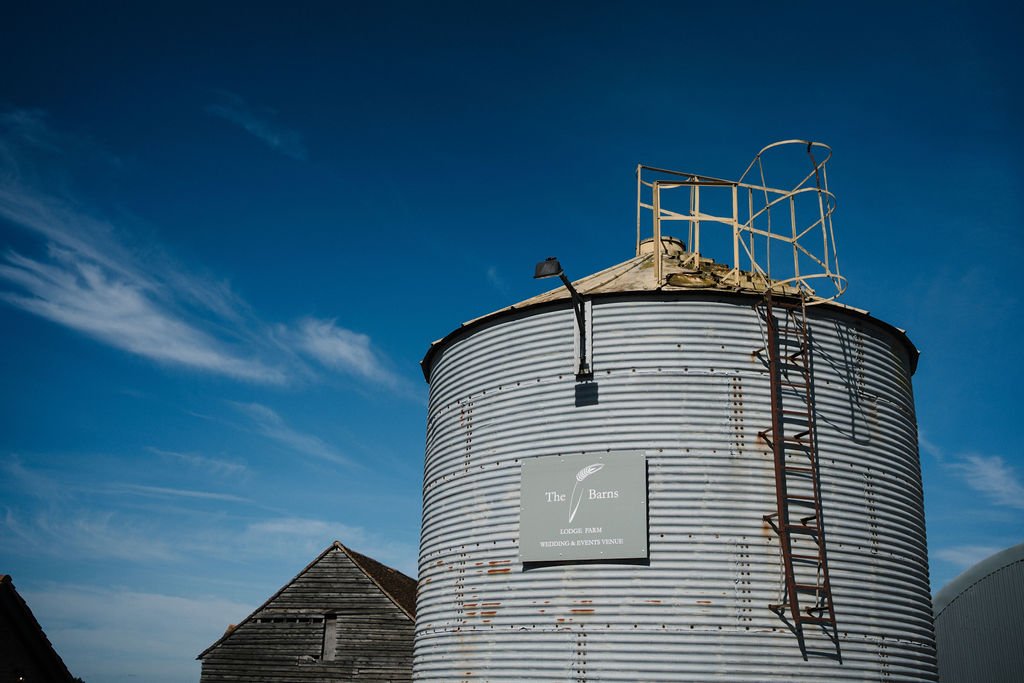 A large rusty corrugated metal silo with a ladder and a deck on top, against a blue sky with wispy clouds.